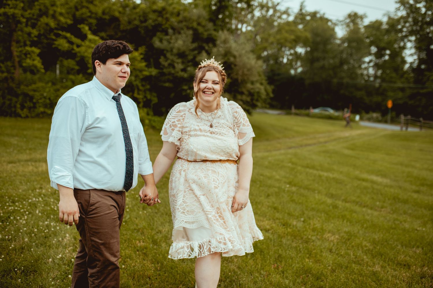 A couple walks together on grassy hillside during golden hour at sunset.