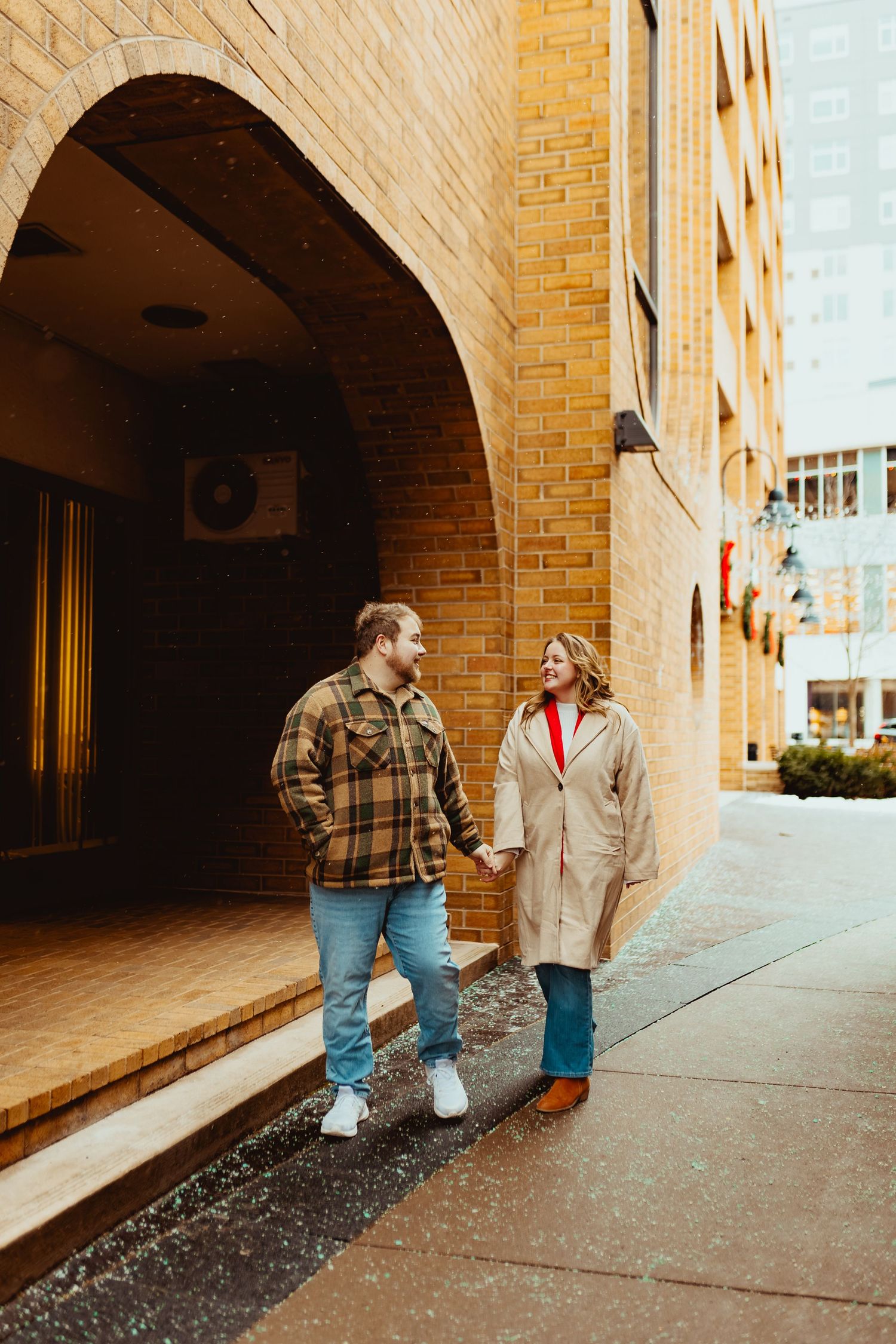 Two people walk together under brick archways of a building exterior.