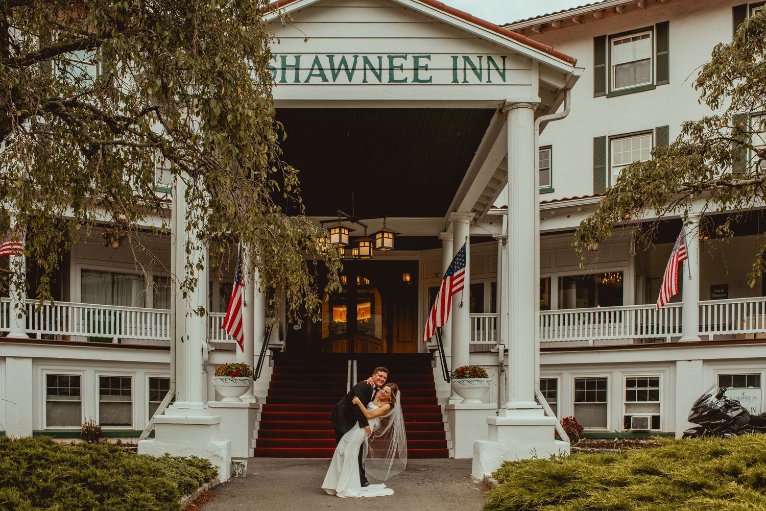 Exterior view of the historic Hawnee Inn, a white colonial-style hotel with wrap-around porches and American flags.