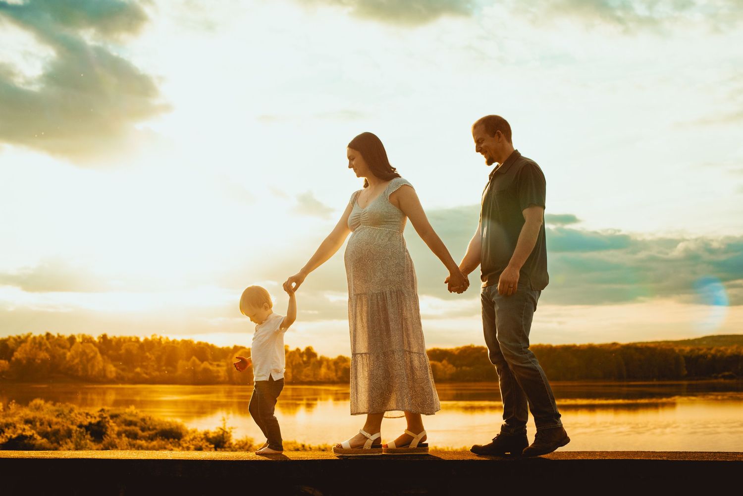 Silhouetted family walking together at sunset along a beach path with golden sunlight streaming through clouds.