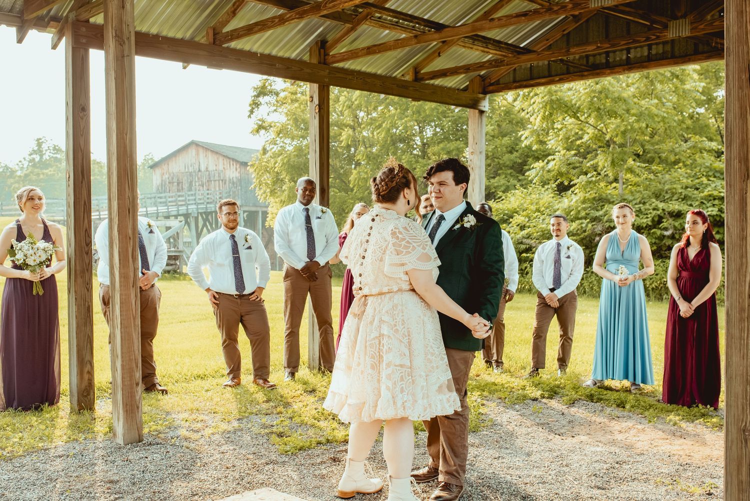 Wedding party stands in formation under a rustic wooden pavilion with natural outdoor scenery in the background.