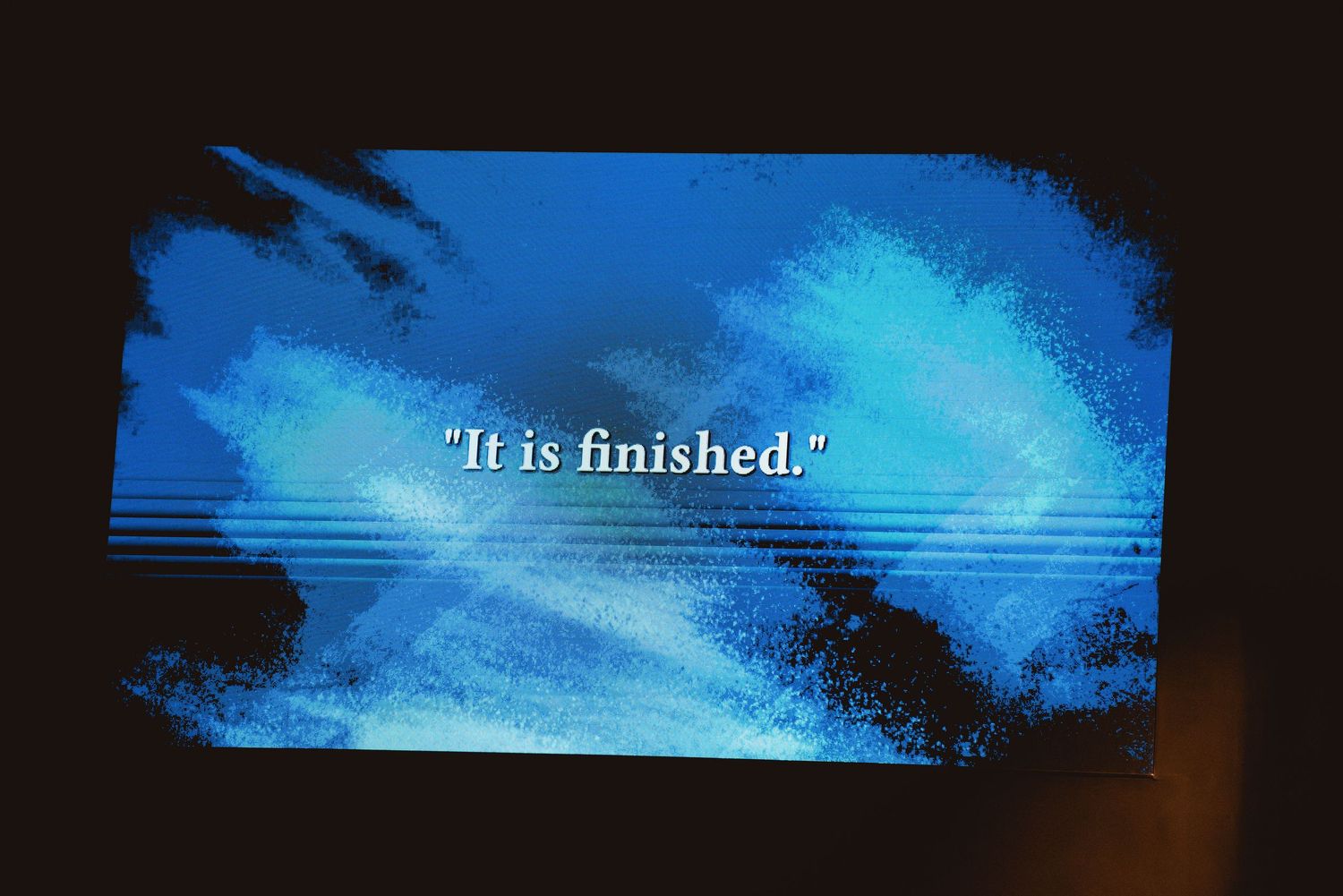 A blue digital display screen shows the text 'It is finished' against a cloudy background.