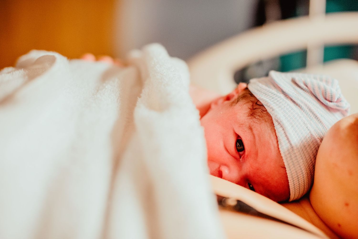 A newborn baby wrapped in white hospital blankets cries while lying on a medical bed.