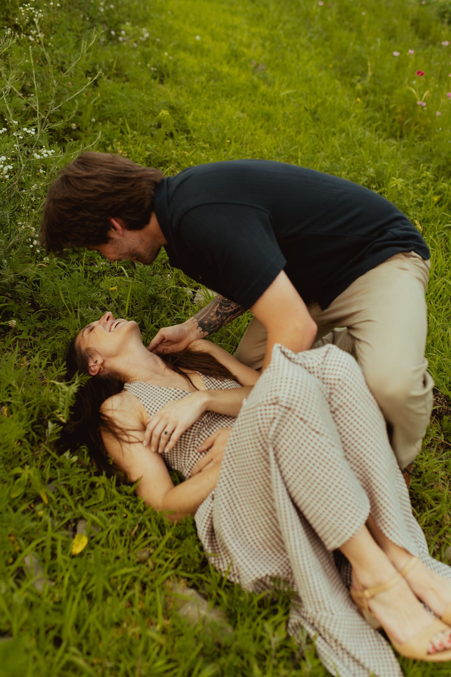 A romantic couple shares a tender moment in a lush green meadow, with a man leaning over a woman lying in the grass.