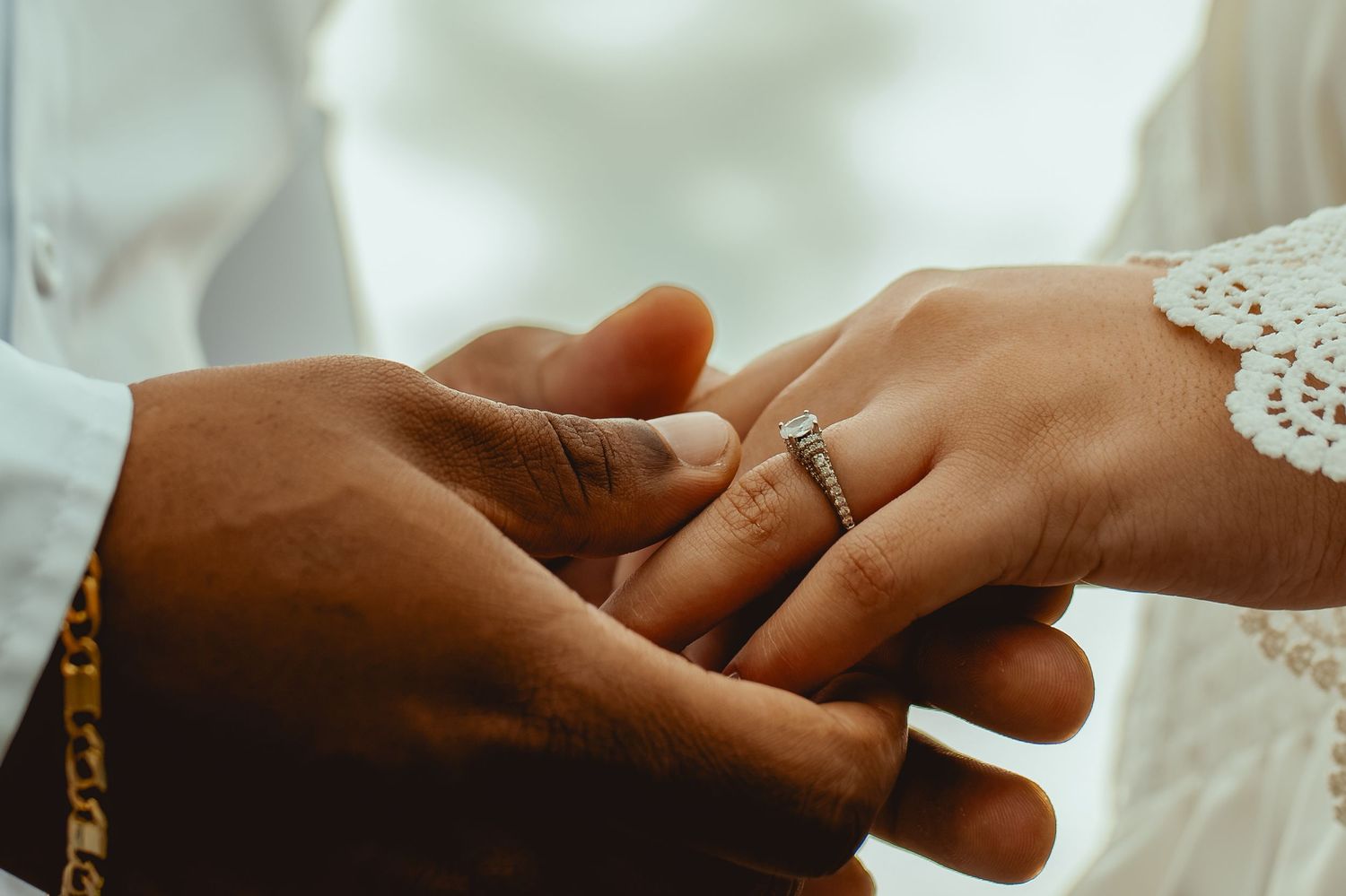 Close-up of groom placing diamond engagement ring on bride's finger during wedding ceremony.