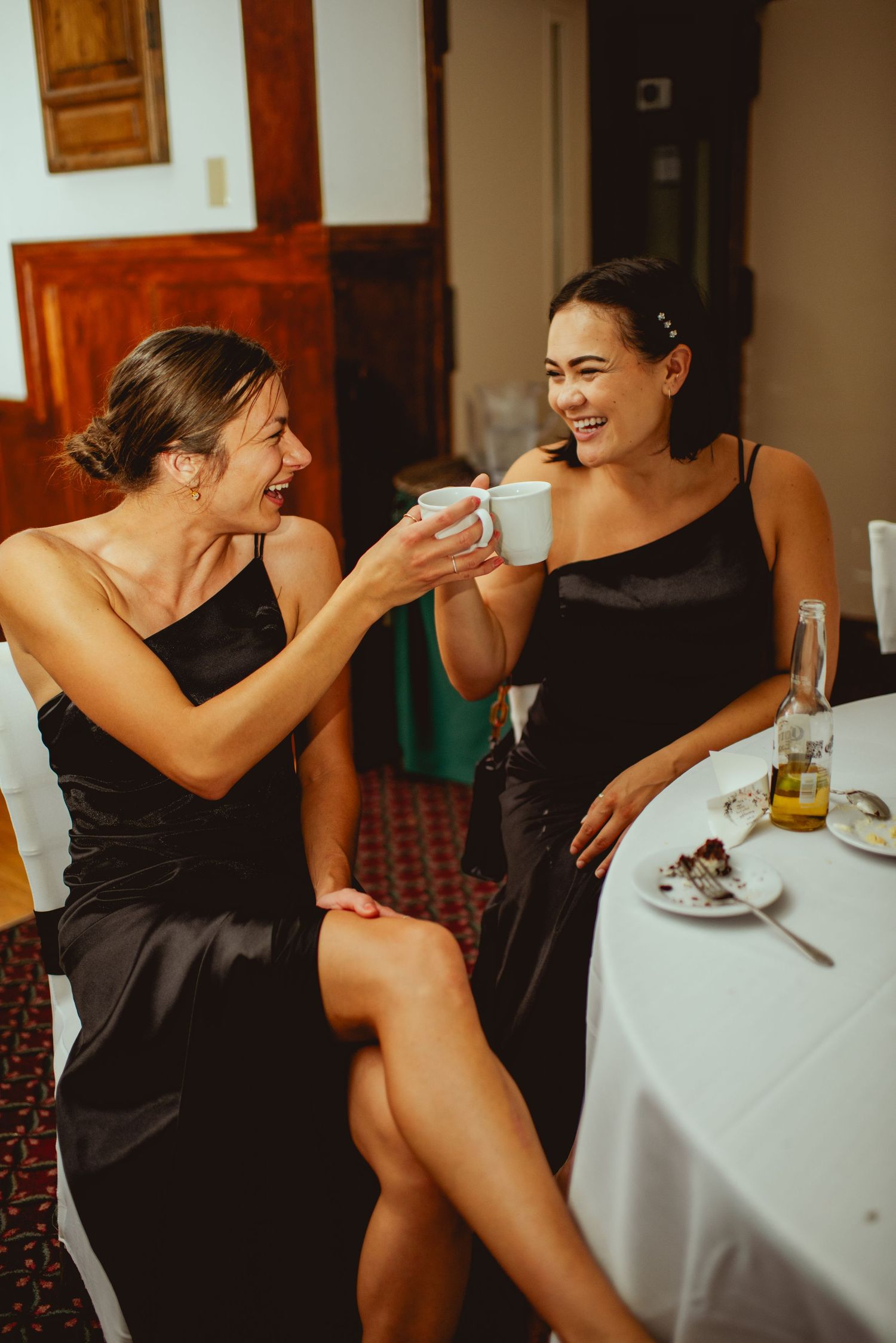 Friends in black dresses sharing laughter and drinks at elegant reception tables.
