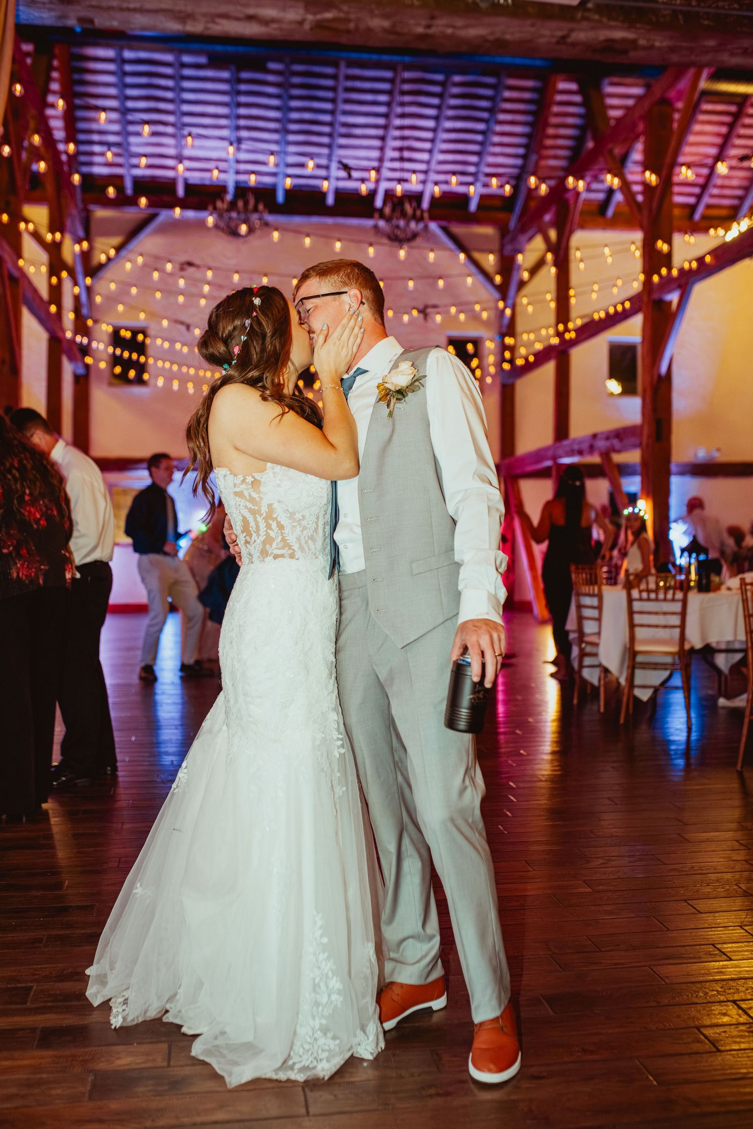 Couple dancing together at a rustic wedding reception venue decorated with warm string lights and wooden beams.