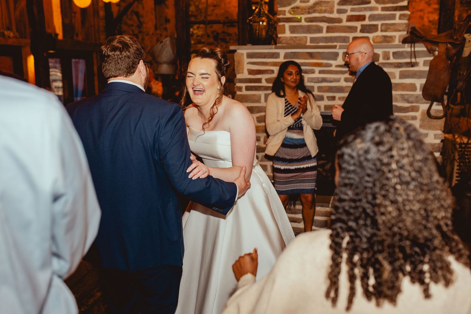 Laughing bride dances with groom as guests celebrate at a rustic stone reception hall.