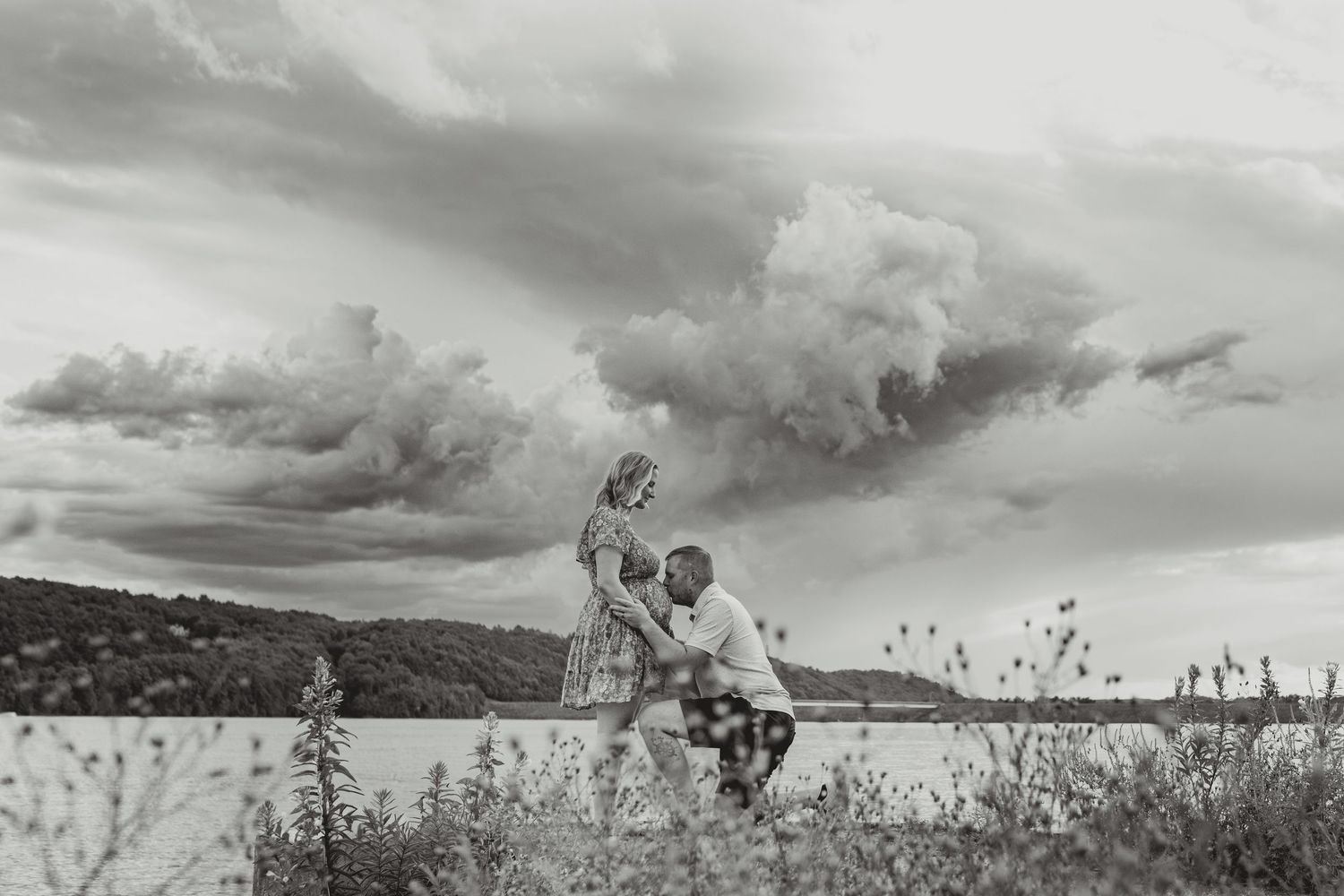Panoramic black and white landscape photograph showing dramatic cloudy skies over a rural mountain vista.