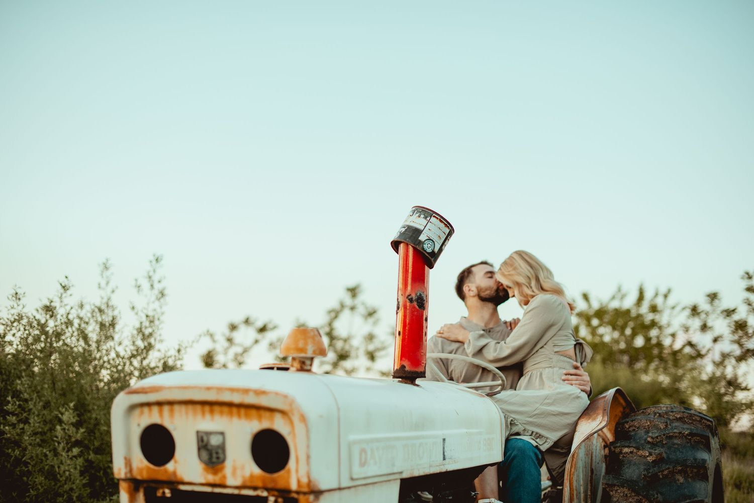 A couple embraces while sitting on a retro blue truck during golden hour.