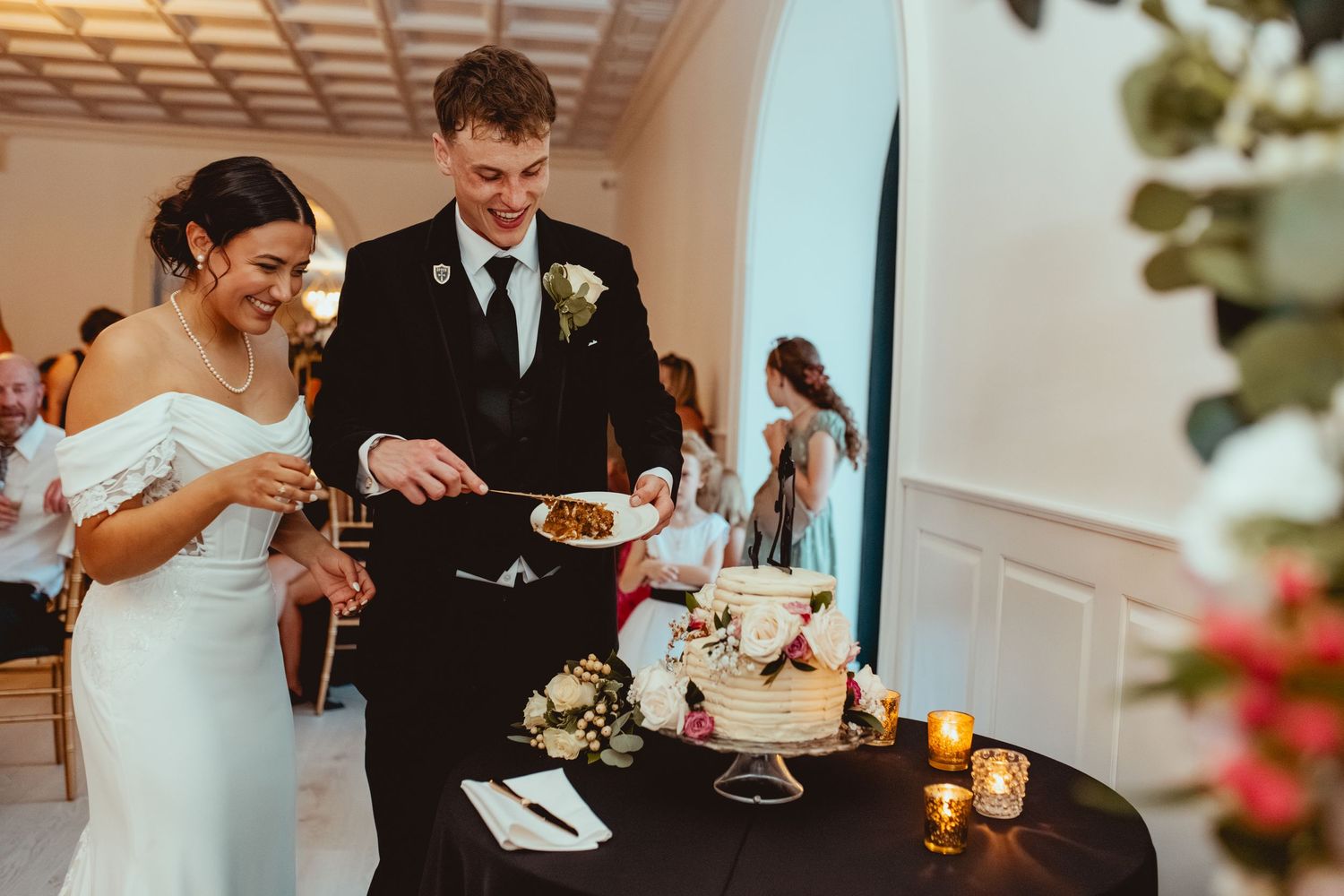 A couple sits together at a reception table enjoying their wedding meal while sharing a laugh.