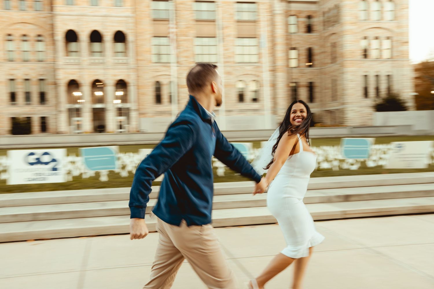 People walking past a grand stone building with fall foliage in warm afternoon light.