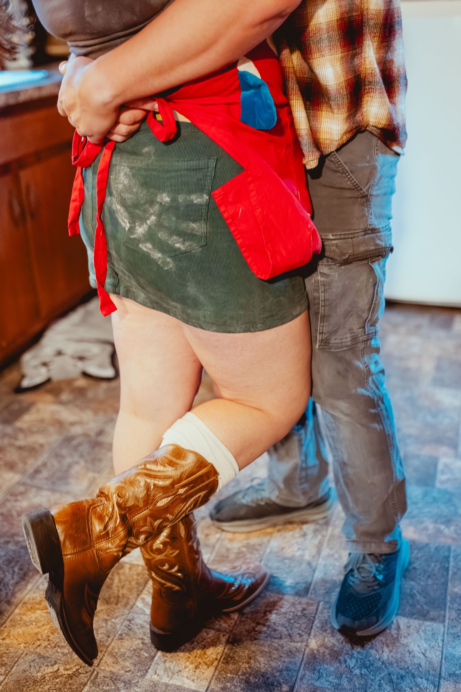 A person wearing brown cowboy boots and red shorts stands on a rustic wooden floor.