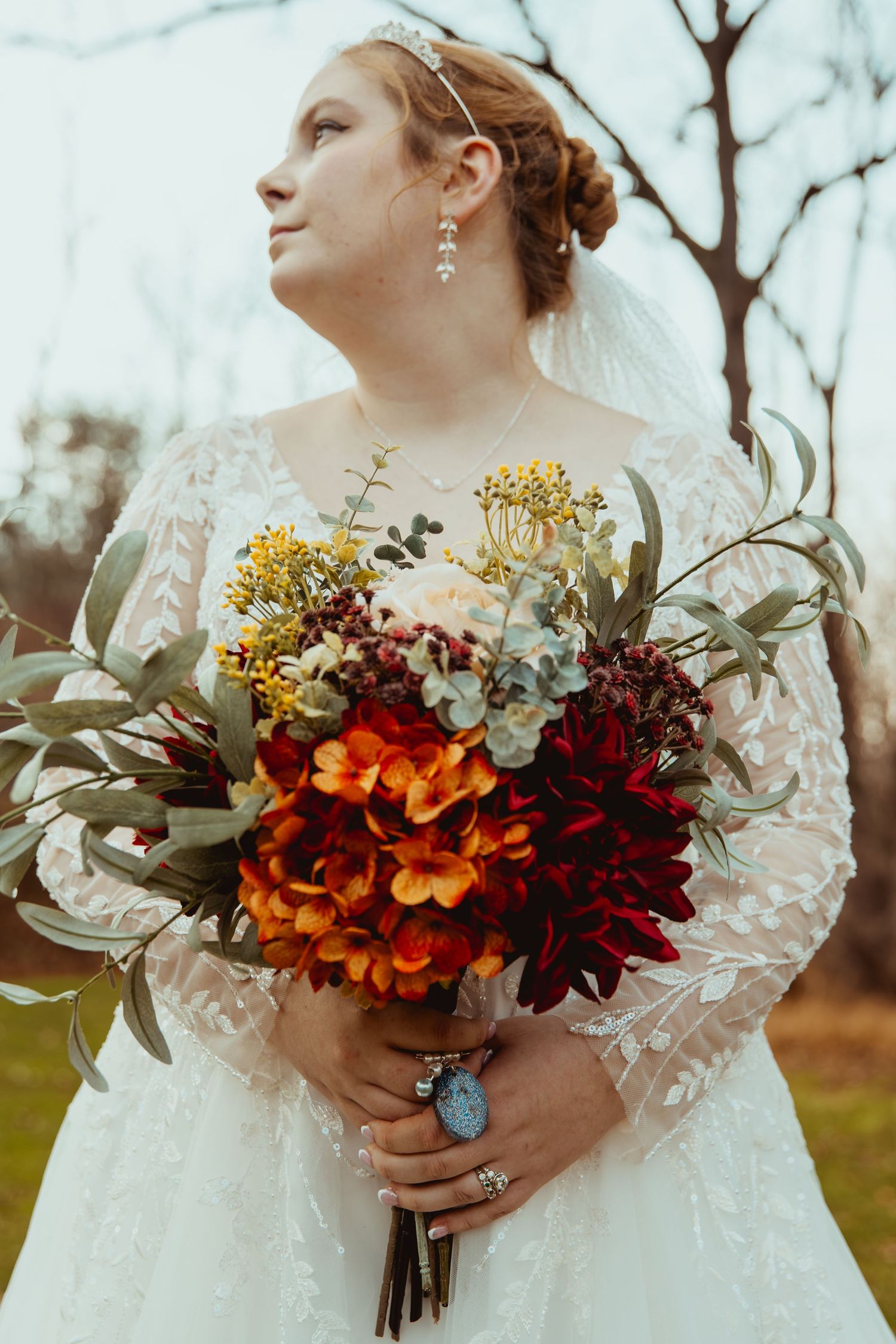 A bridal bouquet featuring vibrant orange, burgundy and yellow flowers paired with a delicate lace wedding dress.