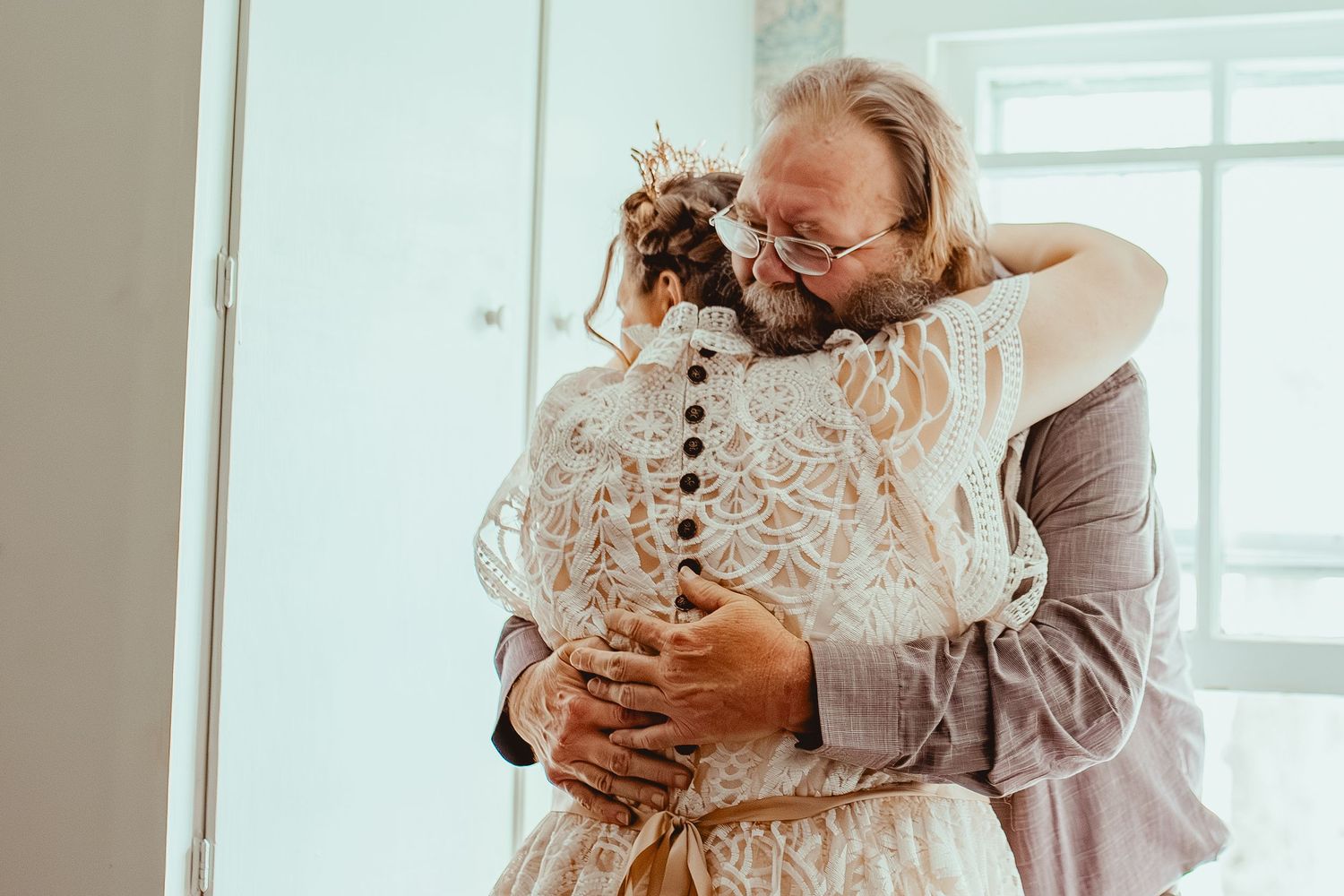 Two people share a joyful embrace at a wedding, with the bride wearing an elegant lace dress.
