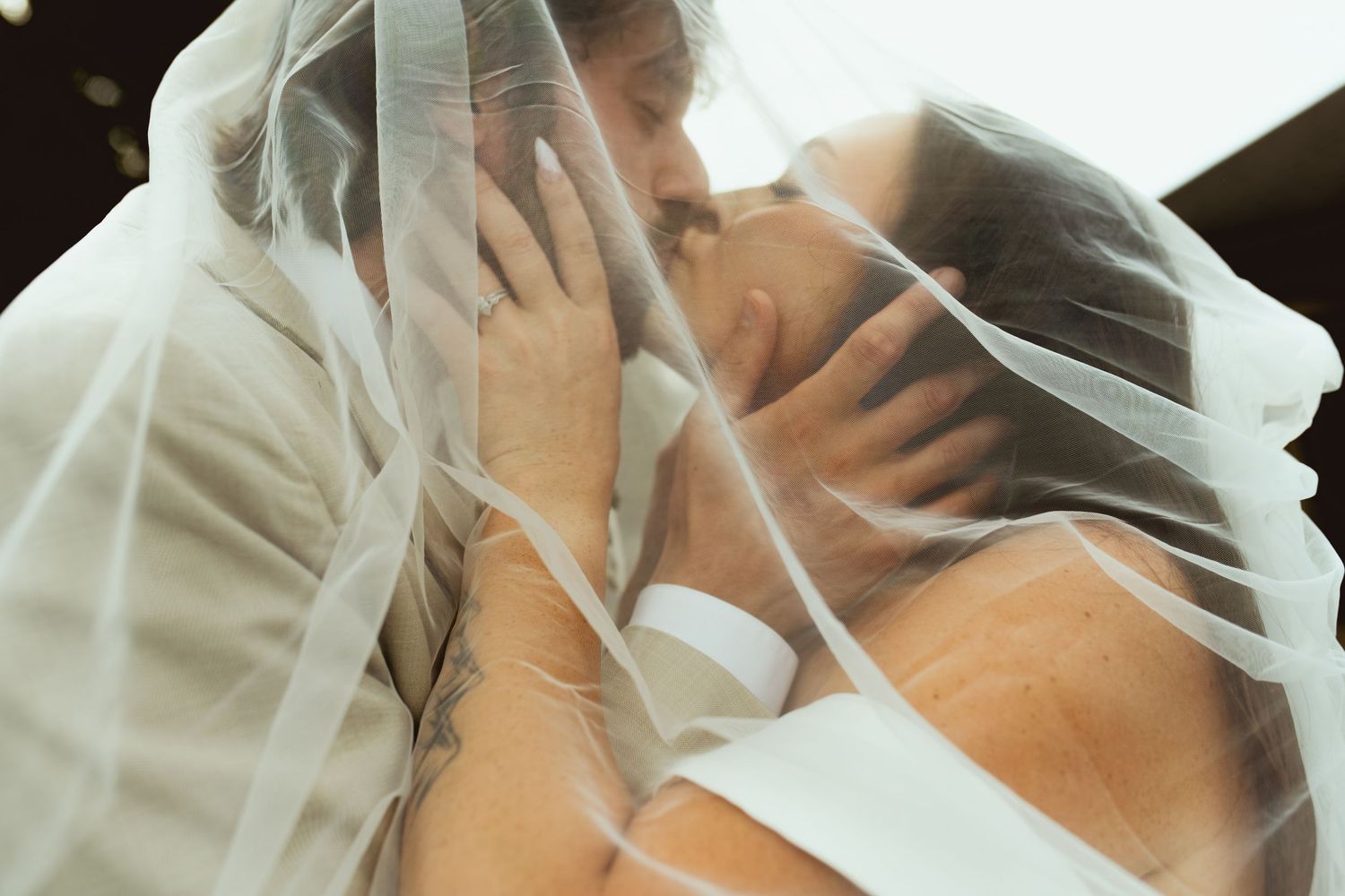 Bride and groom sharing a romantic kiss under a flowing white wedding veil.