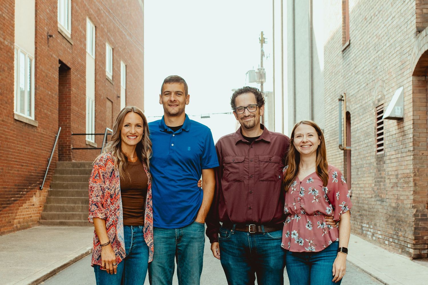 A group of four people standing together in an alley between brick buildings on a sunny day.