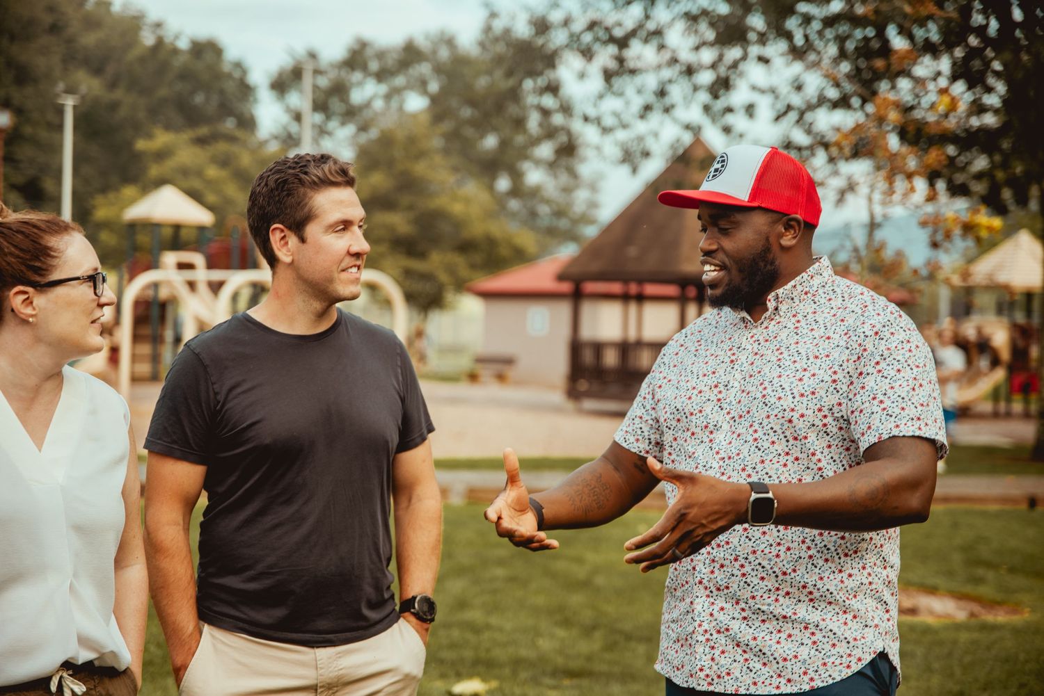 A group of friends plays cornhole outdoors on a sunny day at a park during a casual gathering.
