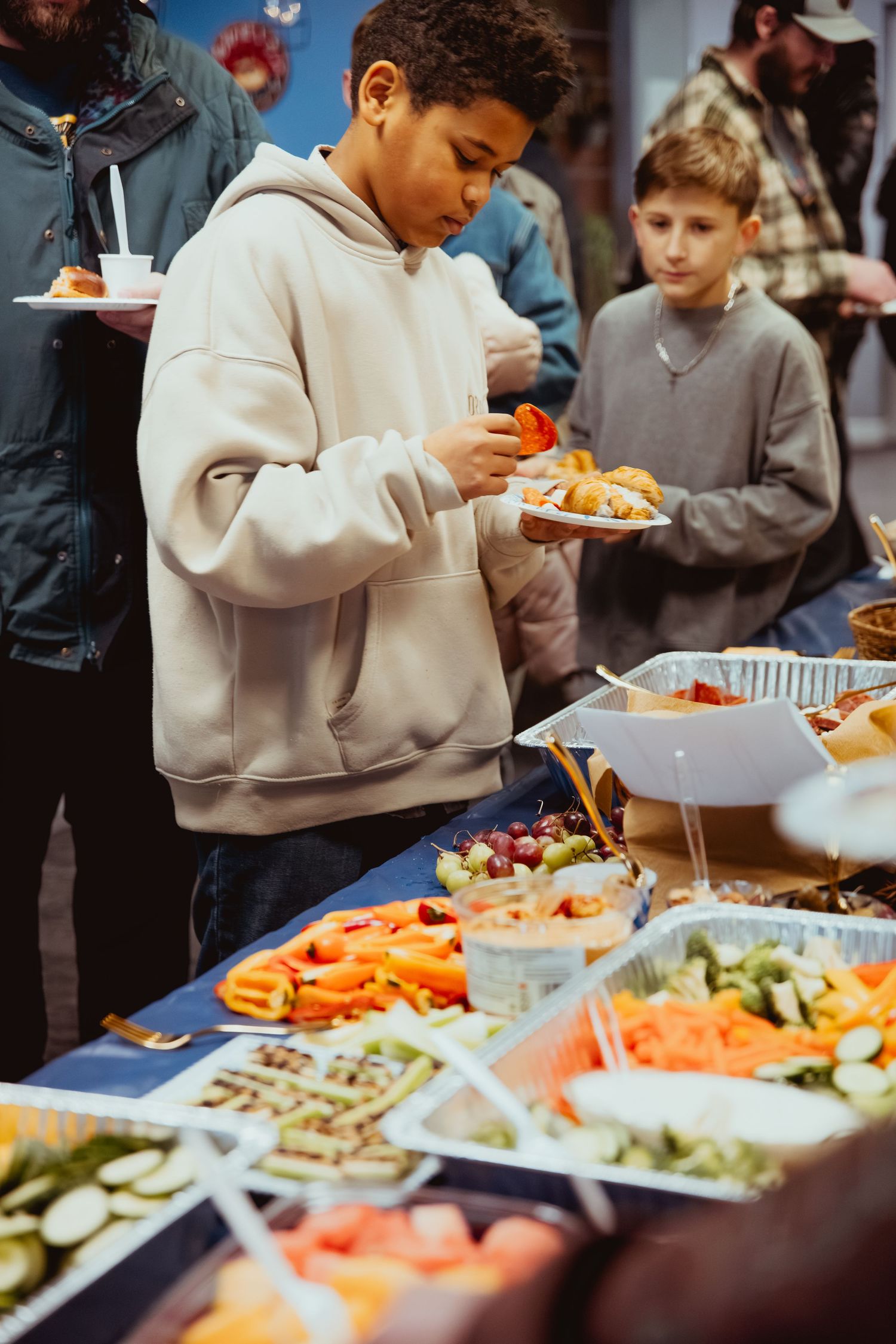 People serving themselves from a buffet line with fresh vegetables and appetizers.