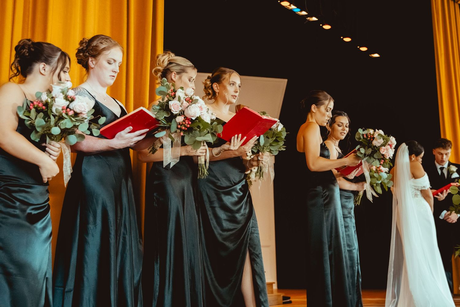 Wedding ceremony lineup against golden curtains in a dark venue.