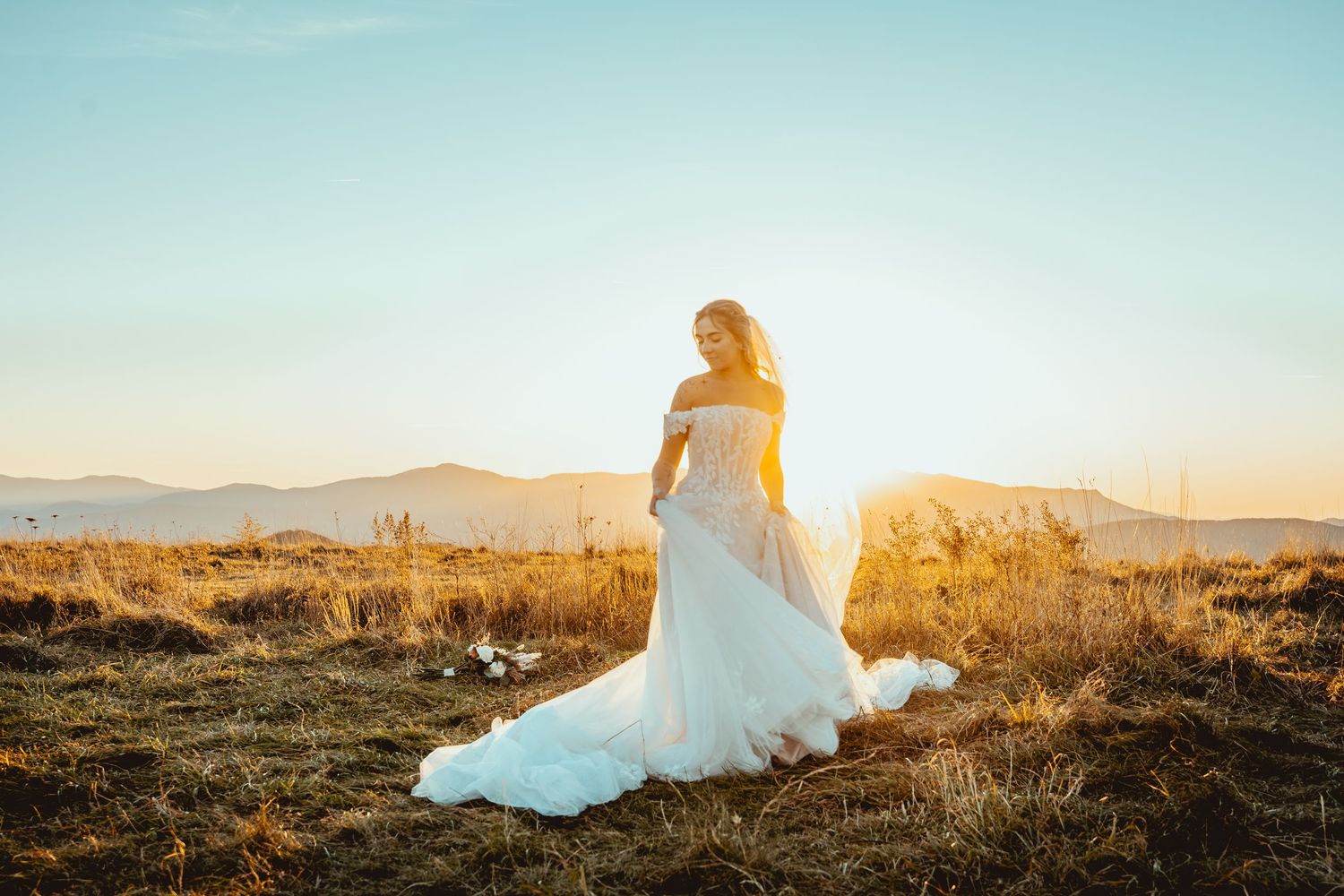 Ethereal bridal portraits at sunset with flowing white dress against desert mountain backdrop.