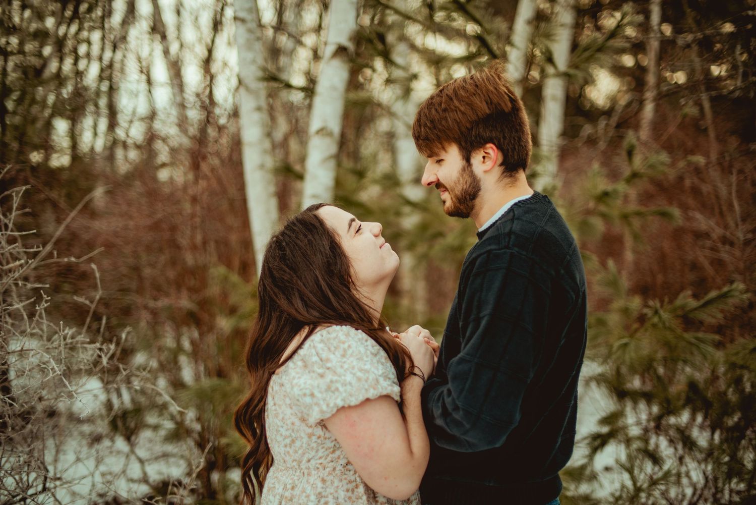 A couple shares an intimate winter moment in a snowy forest setting.
