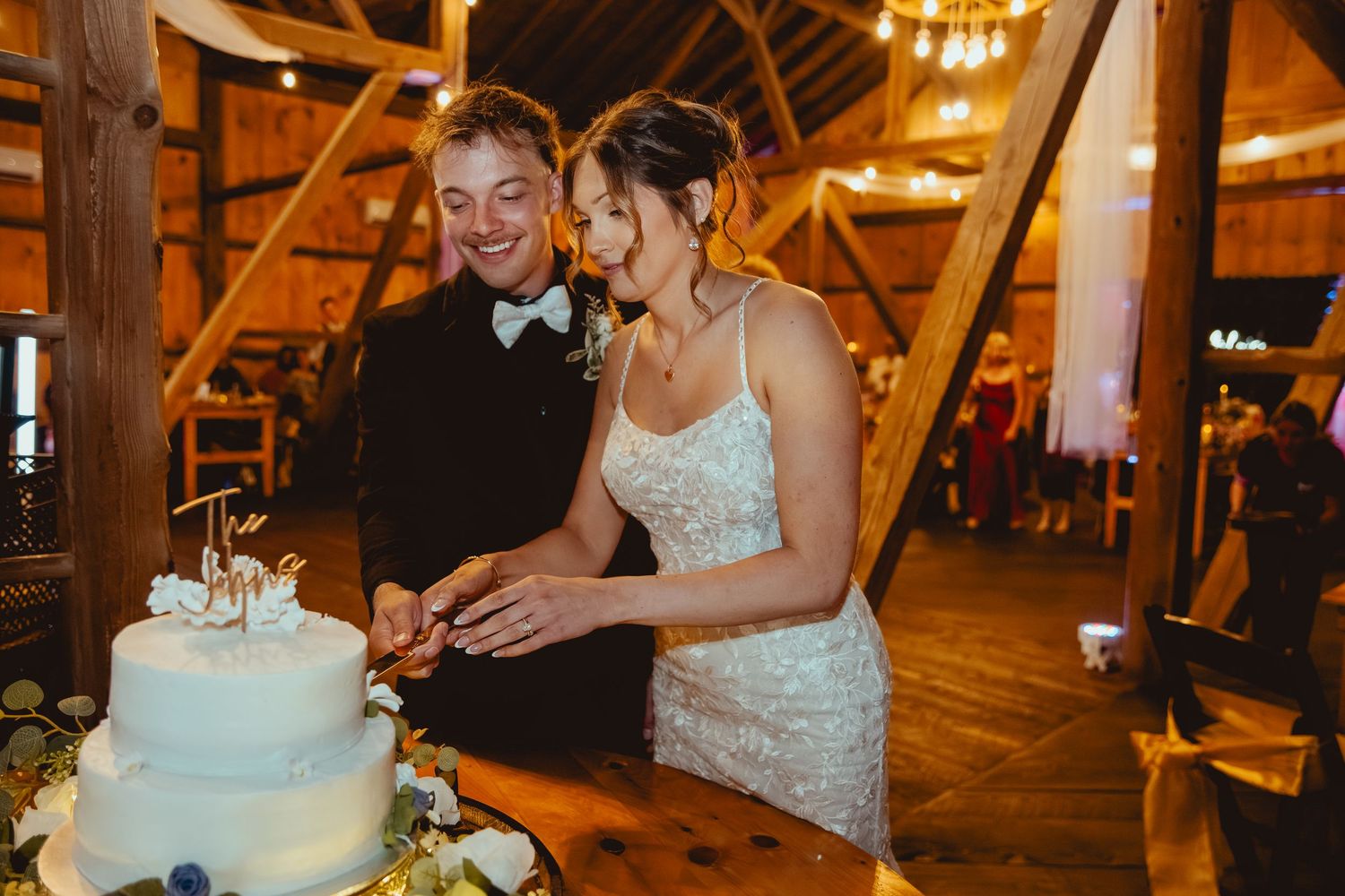 Wedding reception scene in rustic barn venue with warm ambient lighting and elegant table settings.