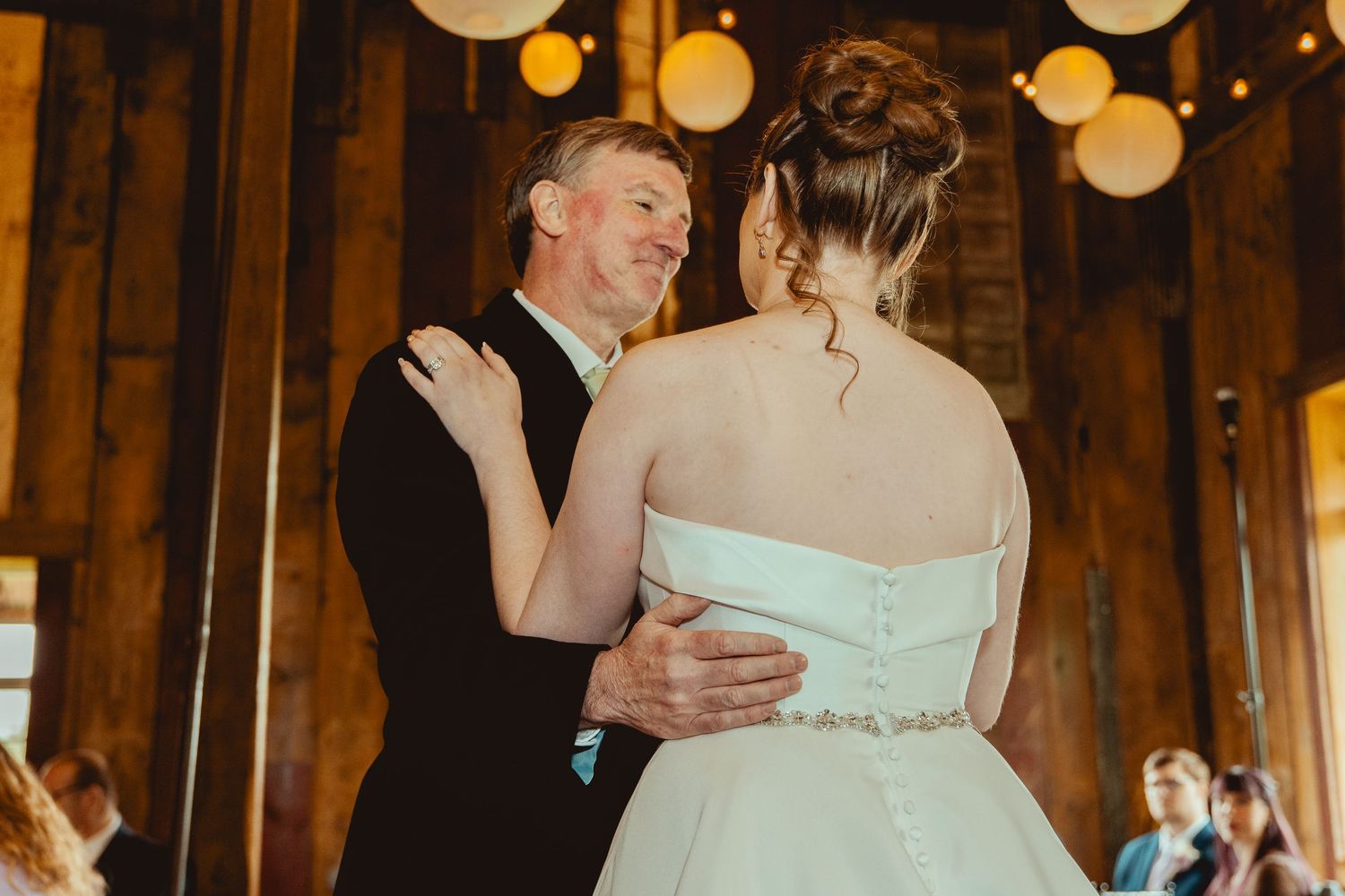 Father daughter dance at rustic barn wedding reception with globe string lights and wooden interior decor.