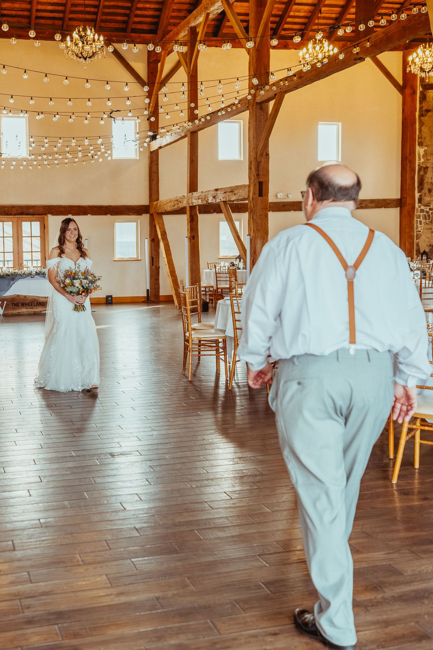 A sequence of photos showing someone in white walking across a rustic wooden barn venue with string lights and chandeliers.