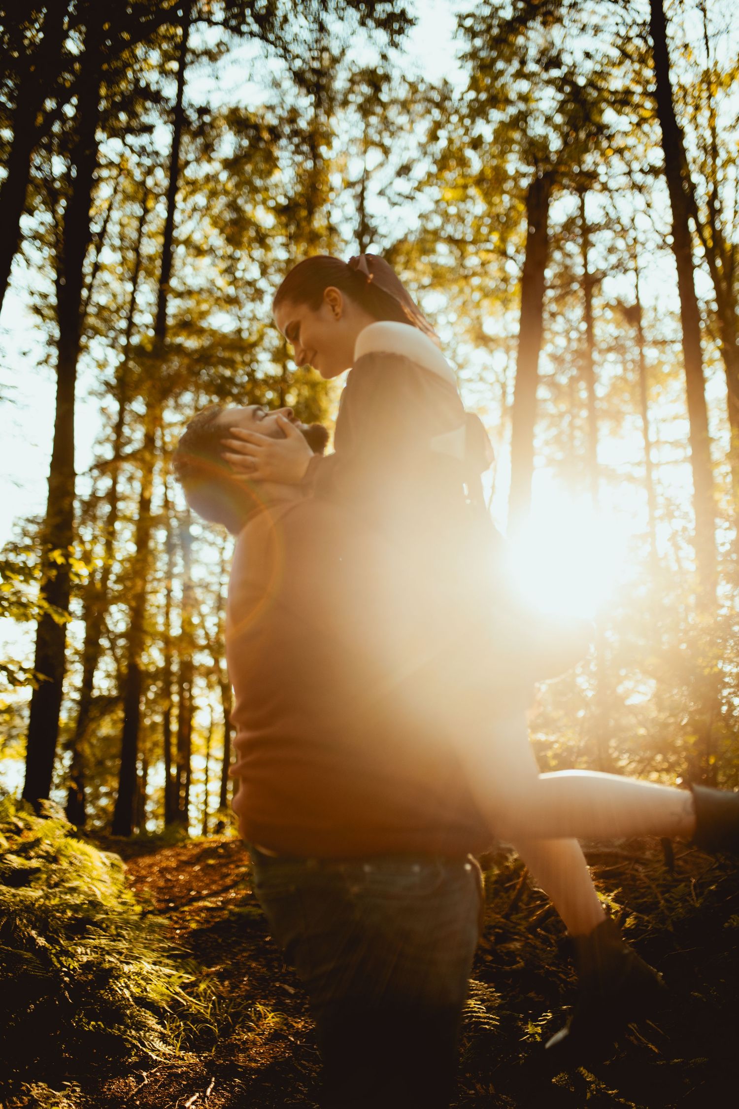 Silhouetted figures embrace in a sunlit forest with golden light streaming through pine trees at sunset.