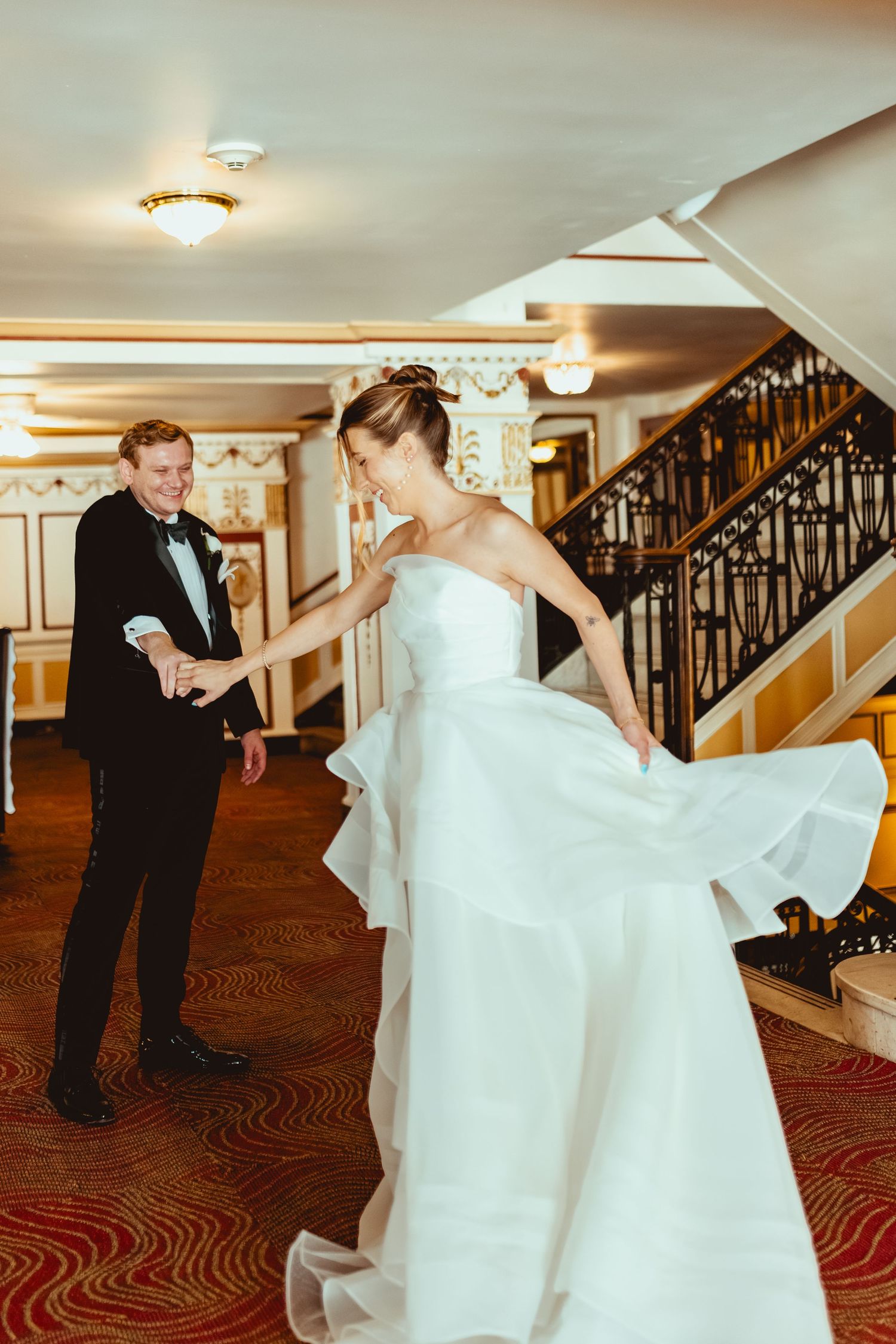 A flowing white wedding dress twirls gracefully near an ornate staircase with wrought iron railings.