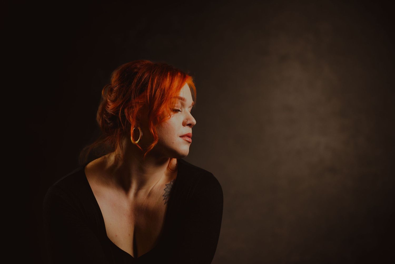 Dramatic portrait with red hair against dark background in moody lighting.