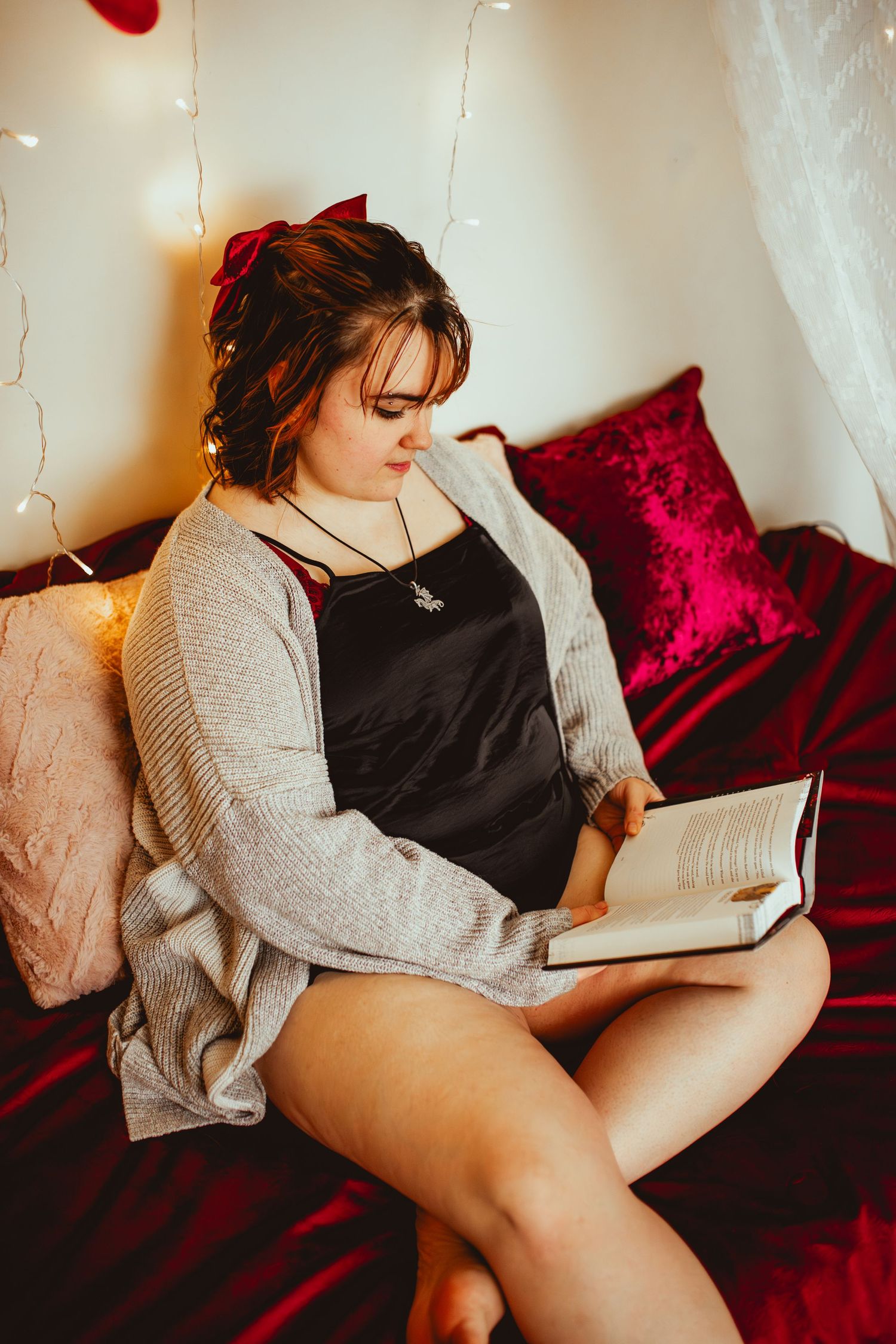 A cozy reading scene with fairy lights and burgundy bedding shows someone relaxing with a book.