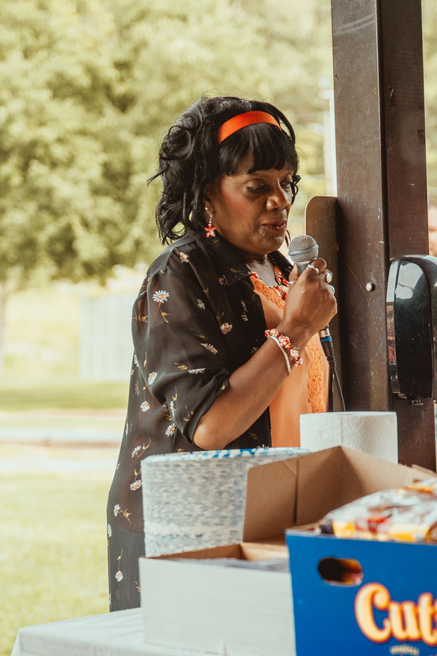 Person enjoying a snack at a covered outdoor picnic area with trees visible in the background.