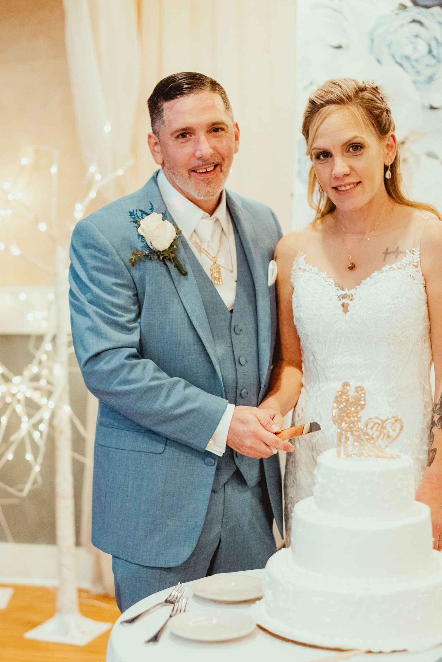 Newlyweds in light blue suit and white wedding dress stand together cutting their elegant white wedding cake.