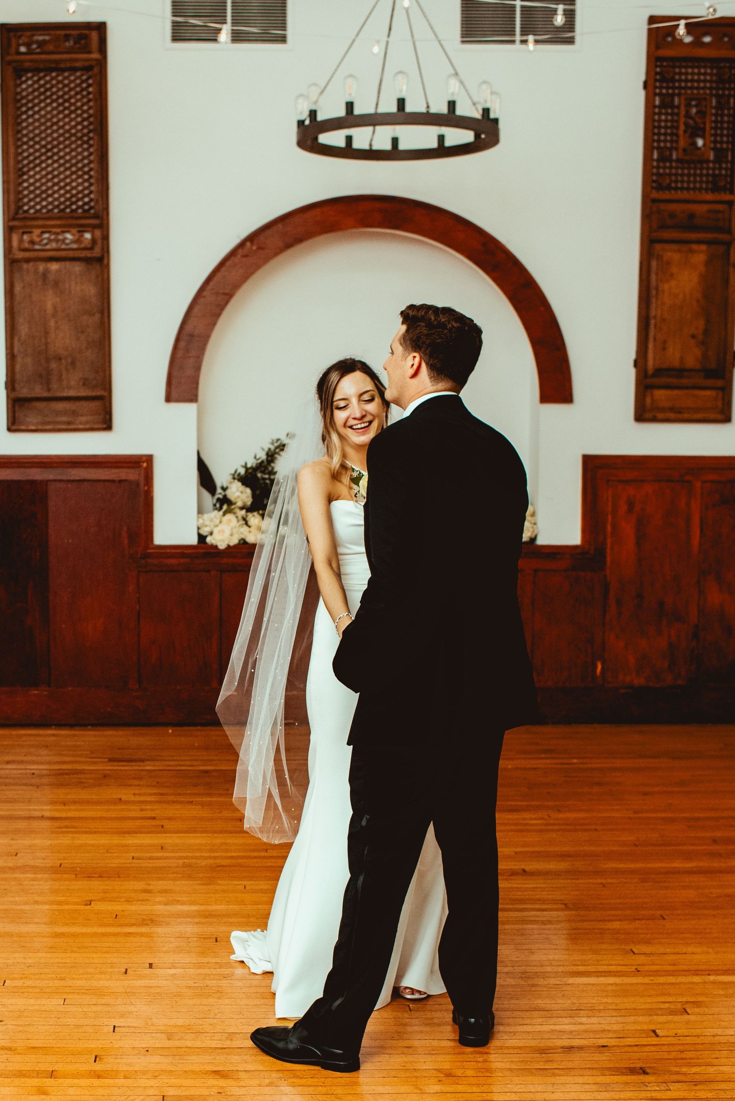 A couple dances together in an elegant reception hall with wooden floors and decorative wall panels.