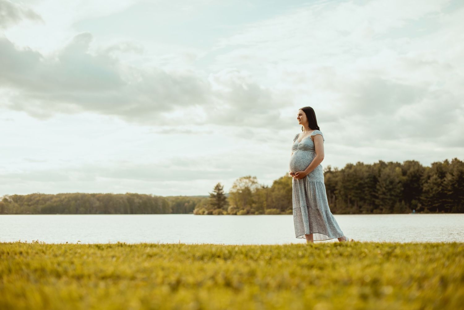 A dreamy maternity photo session in a golden field at sunset with soft lighting and ethereal atmosphere.