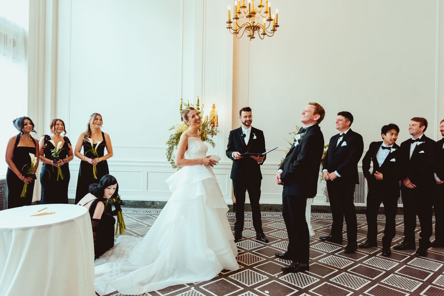 Wedding party members lined up against an elegant white wall in formal attire during celebration.