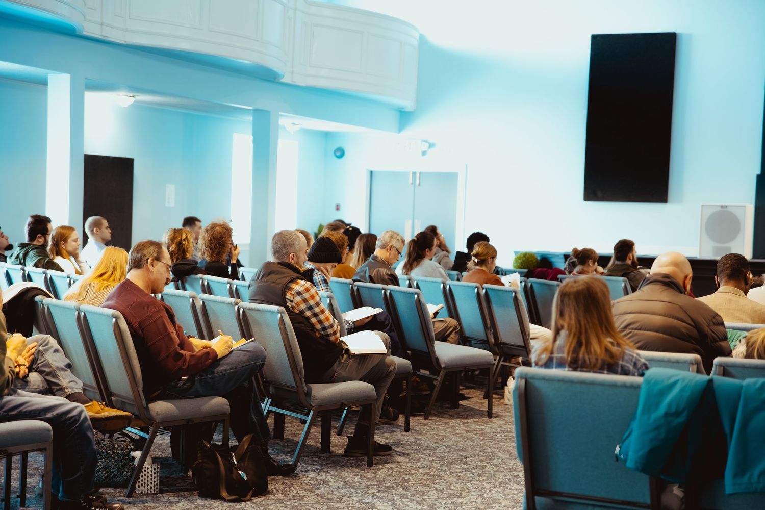 Panoramic view of a modern conference space with teal chairs and audience members.