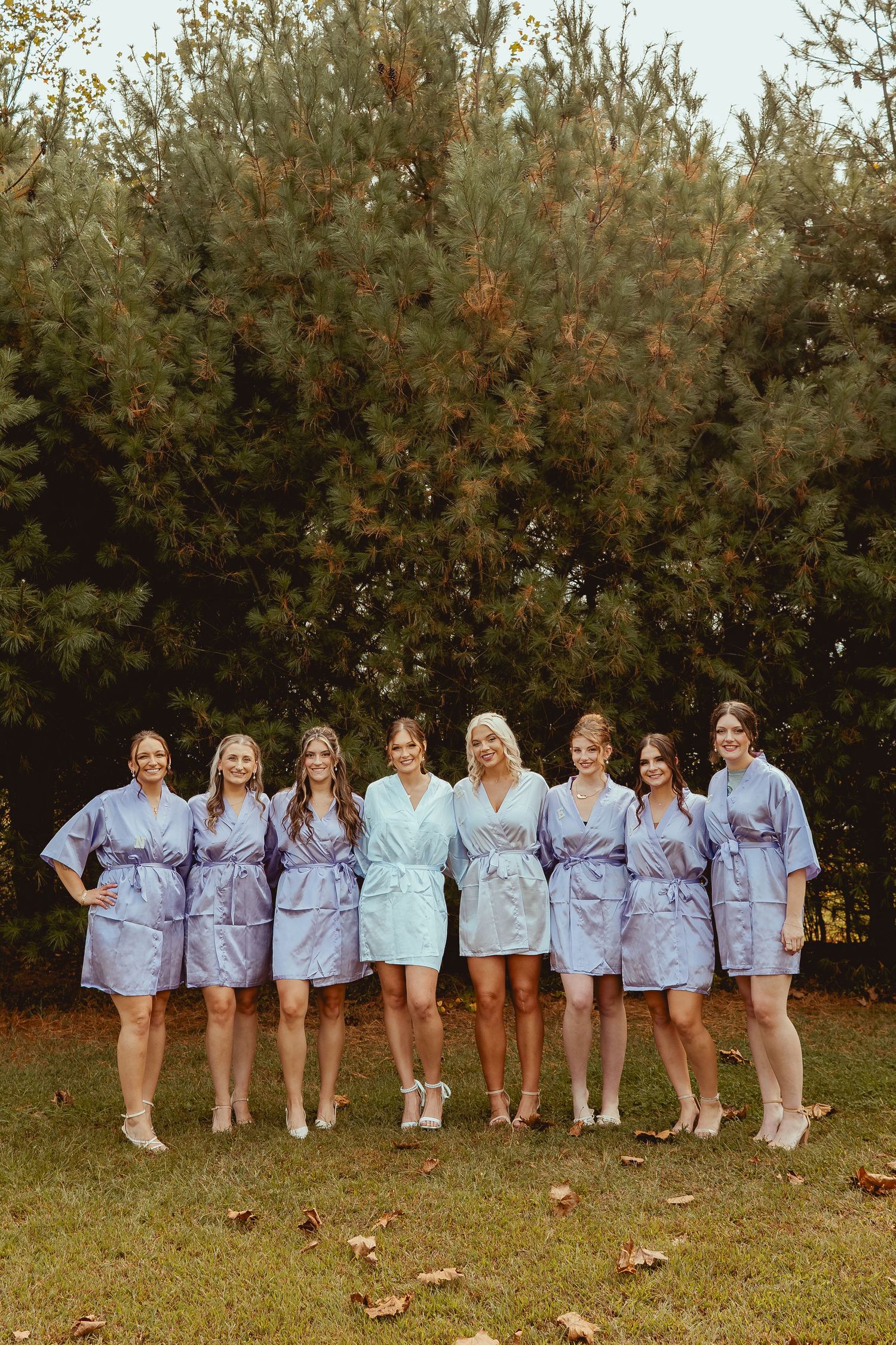 A group wearing matching light blue shirts stands together in a line outdoors during autumn.