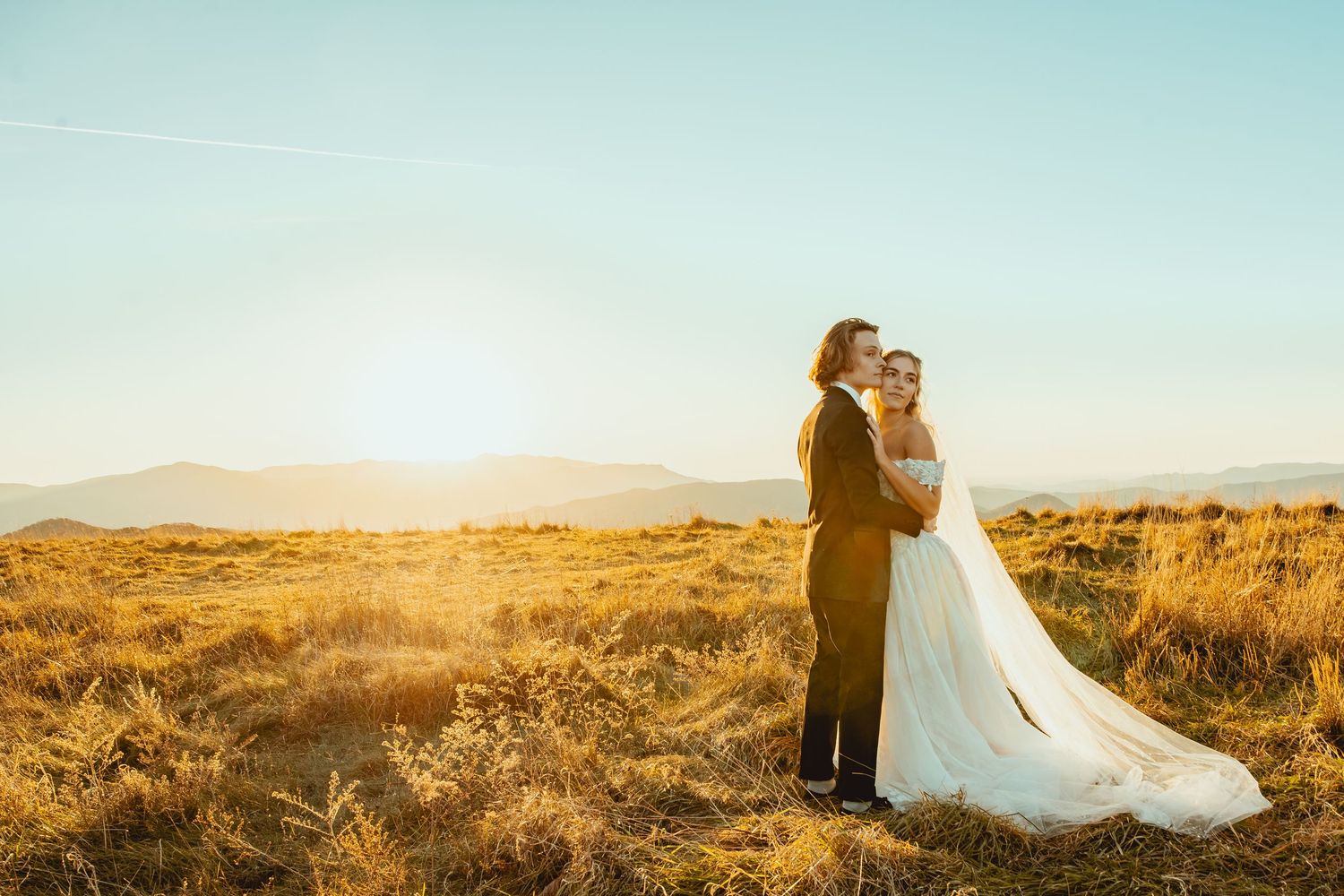 Newlyweds share an intimate moment against a mountainous backdrop during golden hour.
