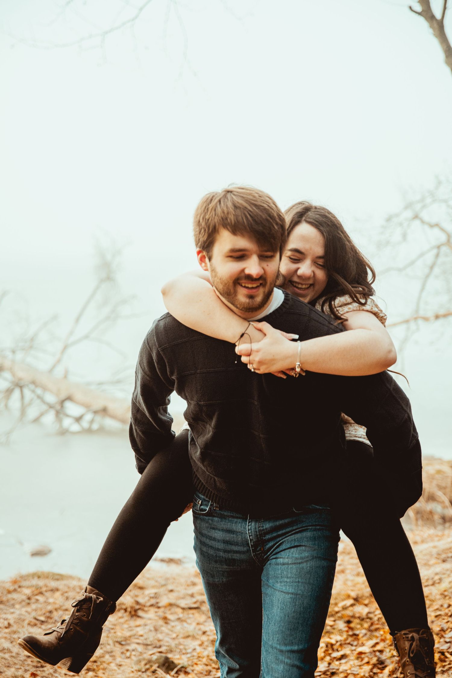 A playful couple shares joyful moments together in autumn leaves during an outdoor photo session.