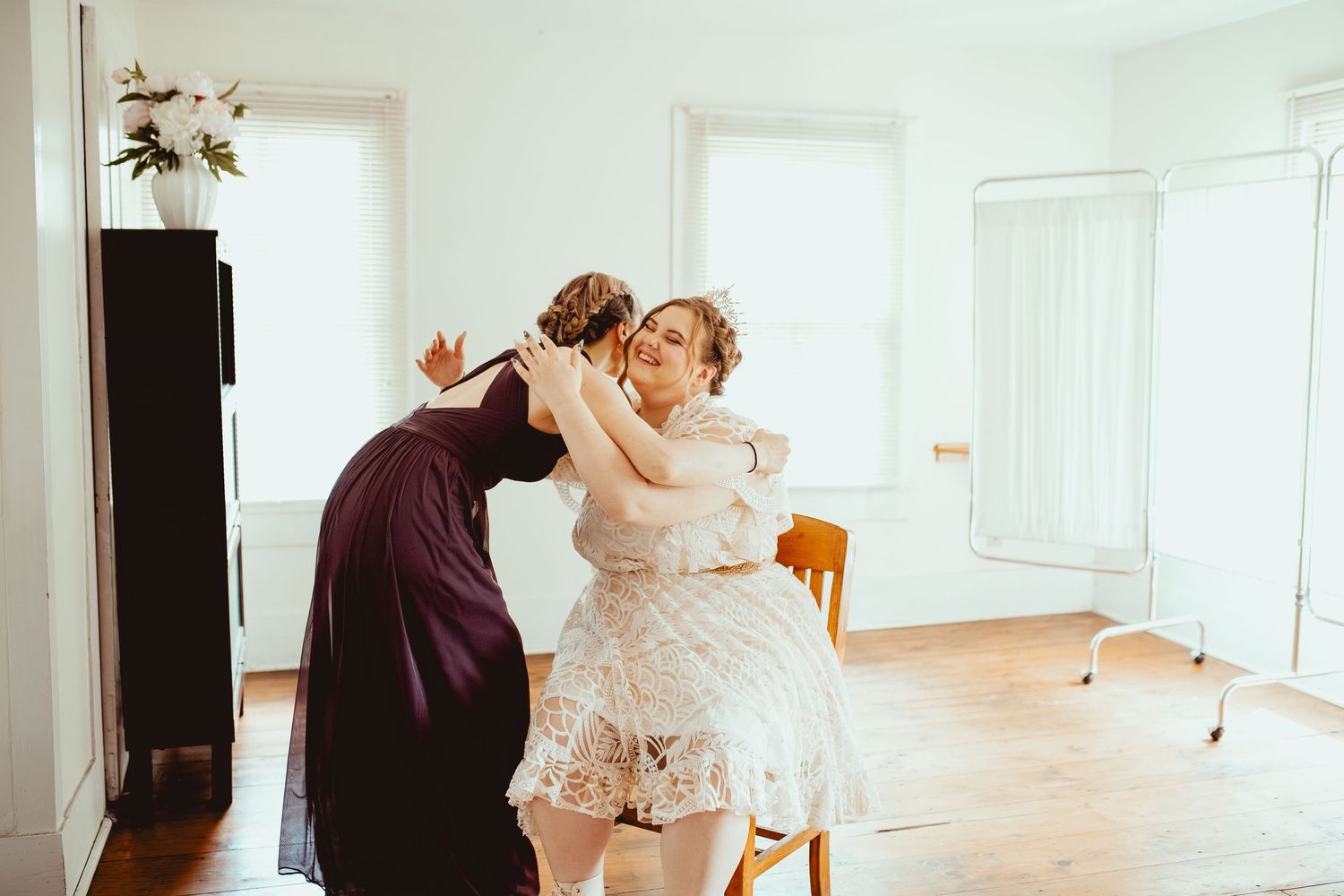 Two people in elegant dresses dance together in a bright white room with hardwood floors.