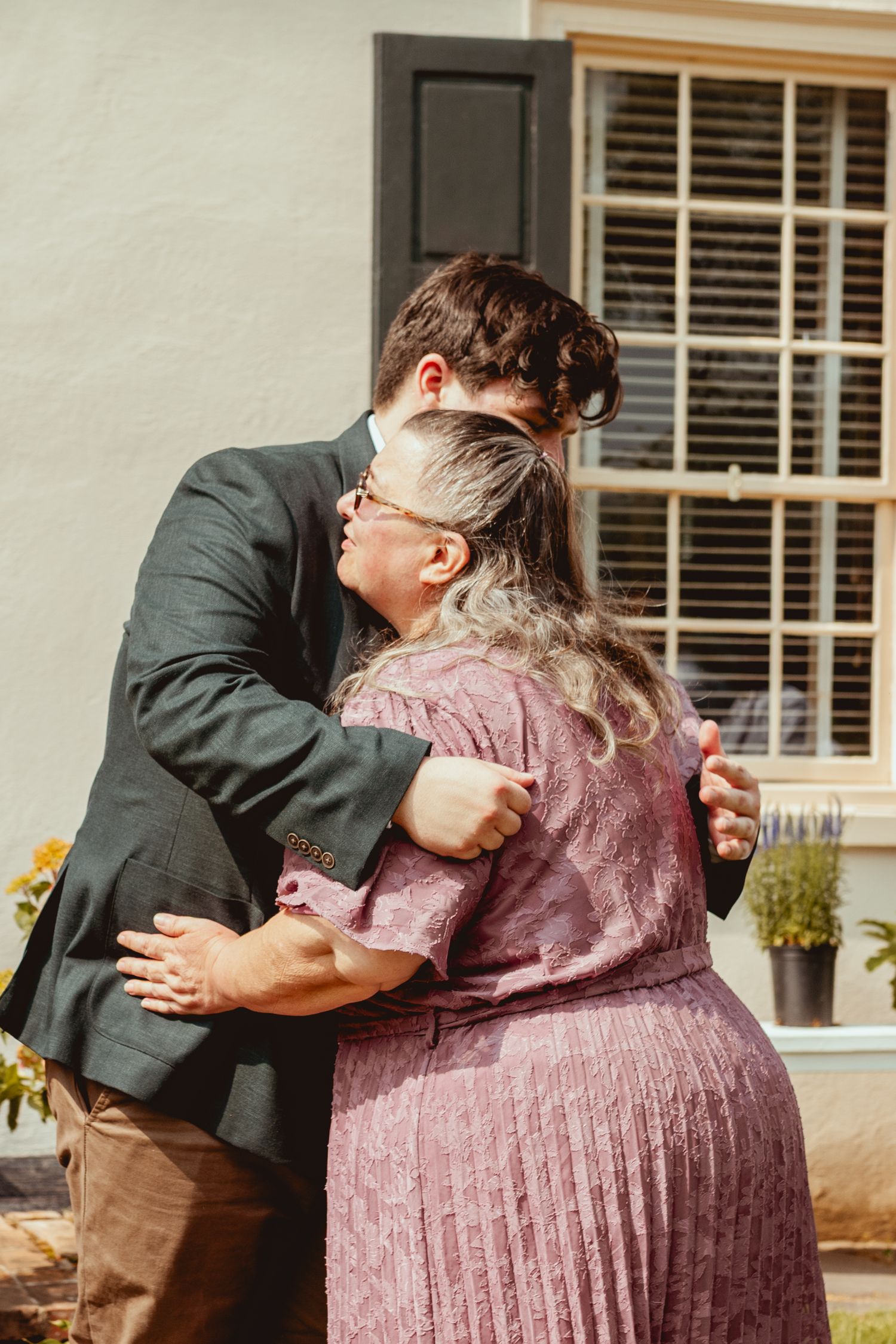 A sequence of four photos showing a couple hugging and embracing in front of a house with white shutters and sunflowers.