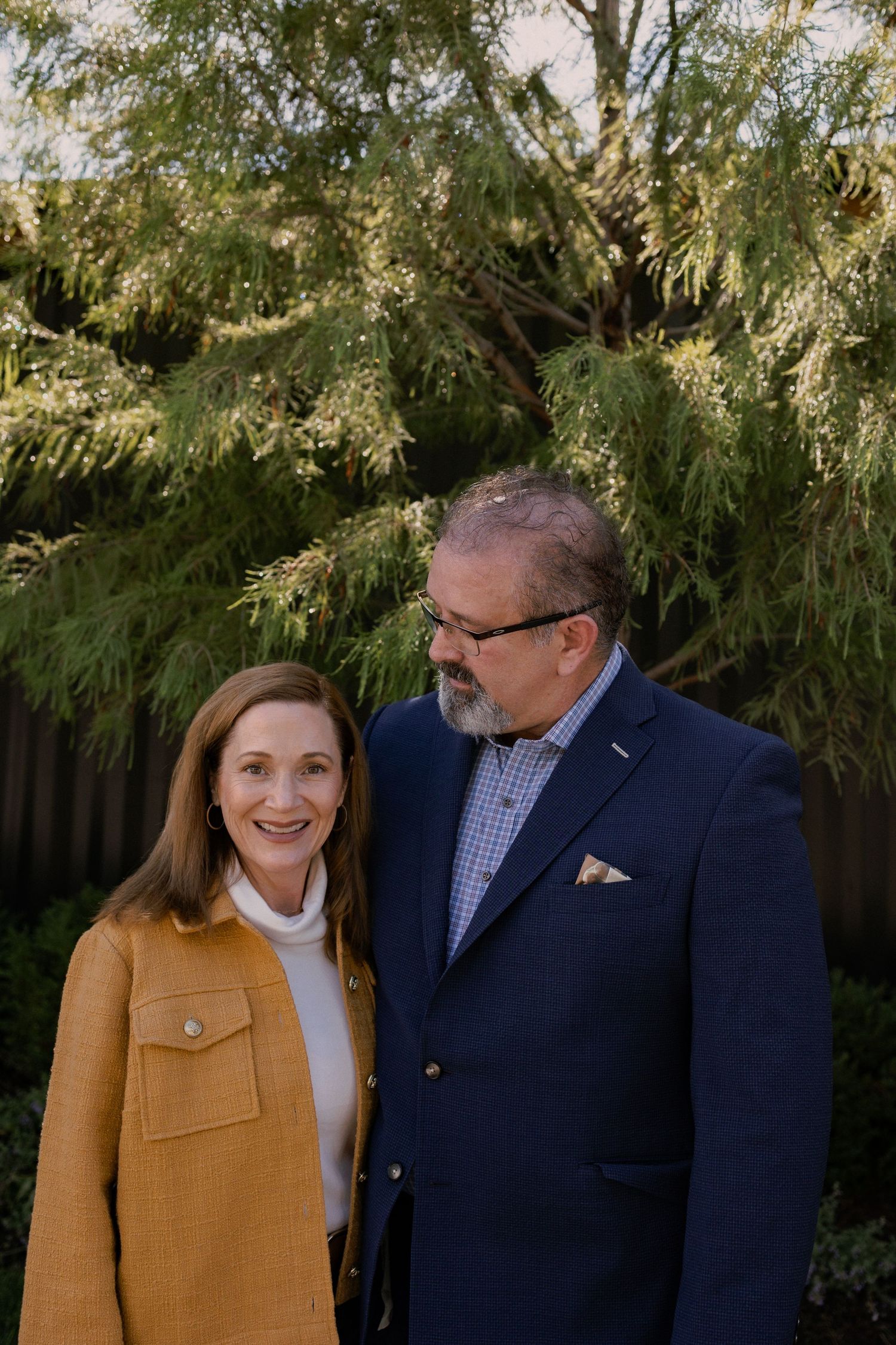 Couple smiling together against backdrop of evergreen trees.