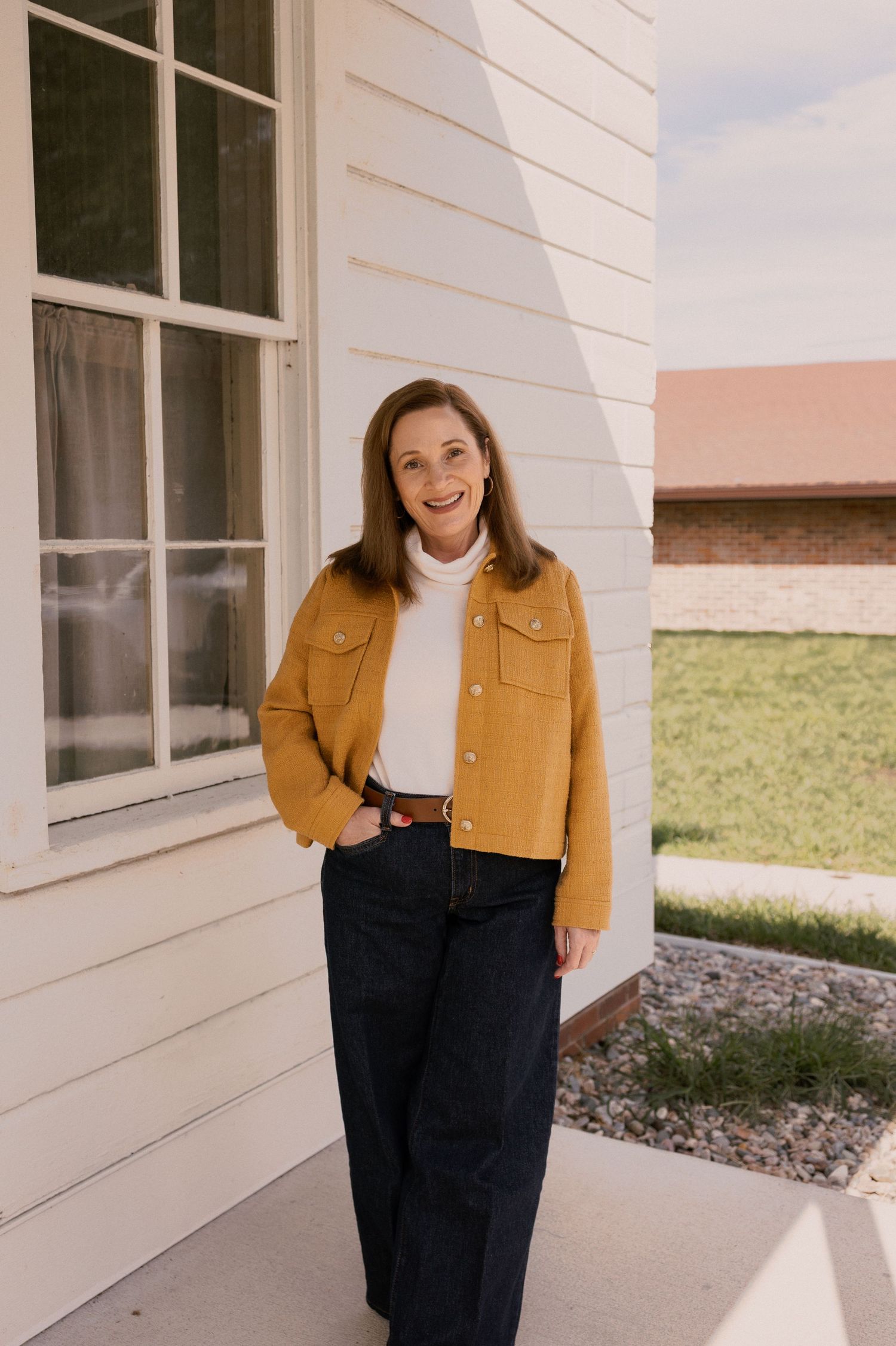 Lifestyle portrait of person in yellow jacket and dark pants on white porch.