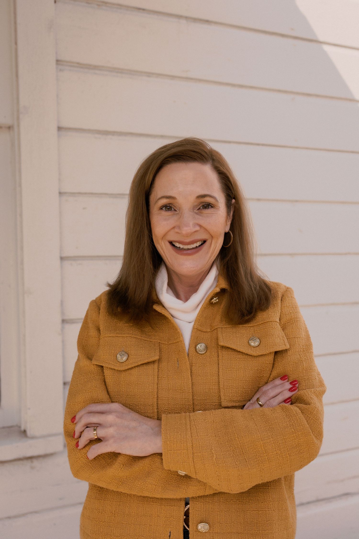 Cheerful portrait of person in yellow jacket against white exterior wall.