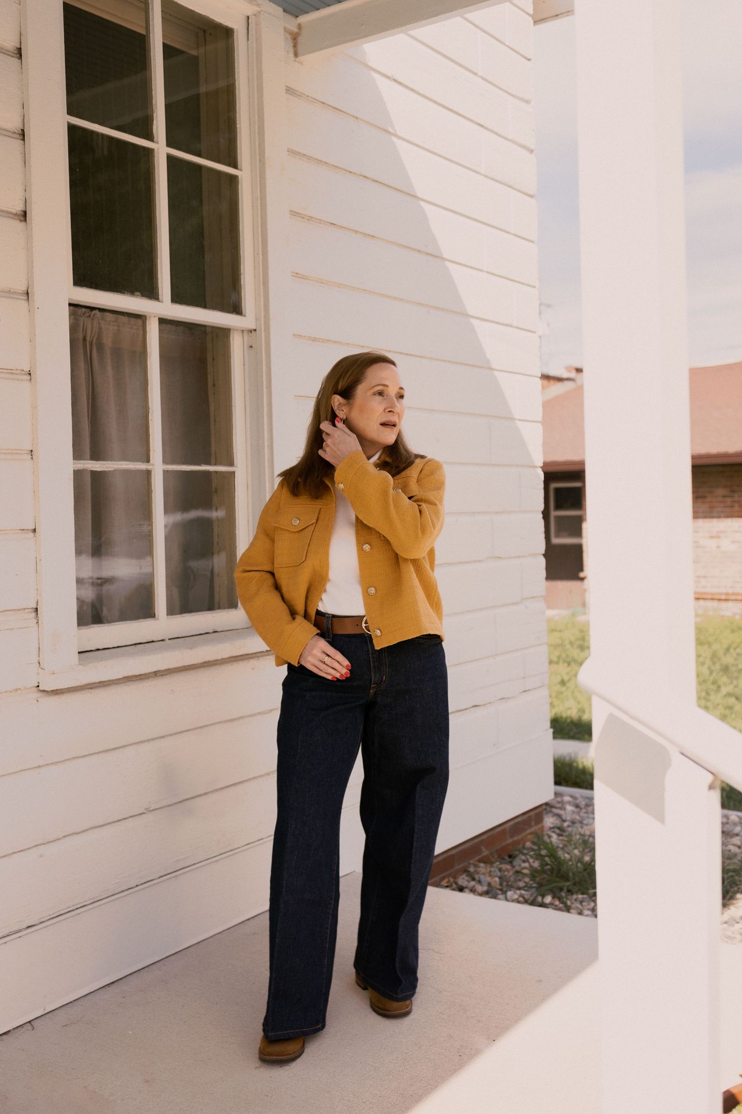 Candid shots of person in mustard jacket posing playfully on white porch.