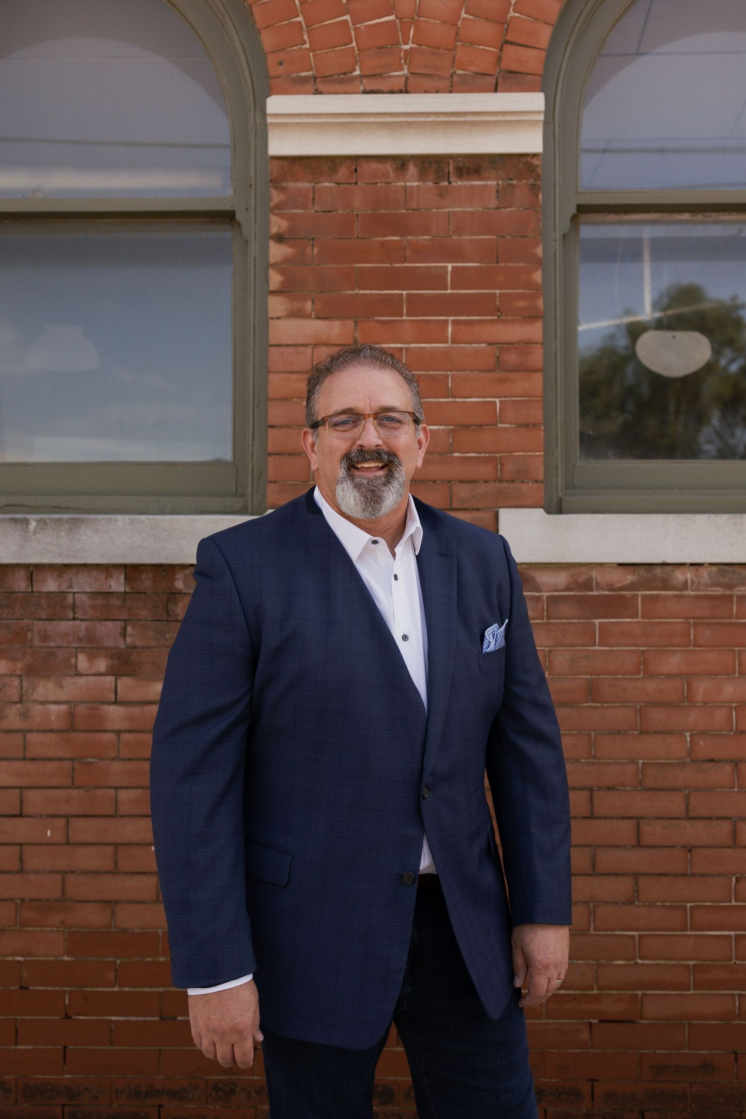 Man in navy suit and pocket square poses against brick building.
