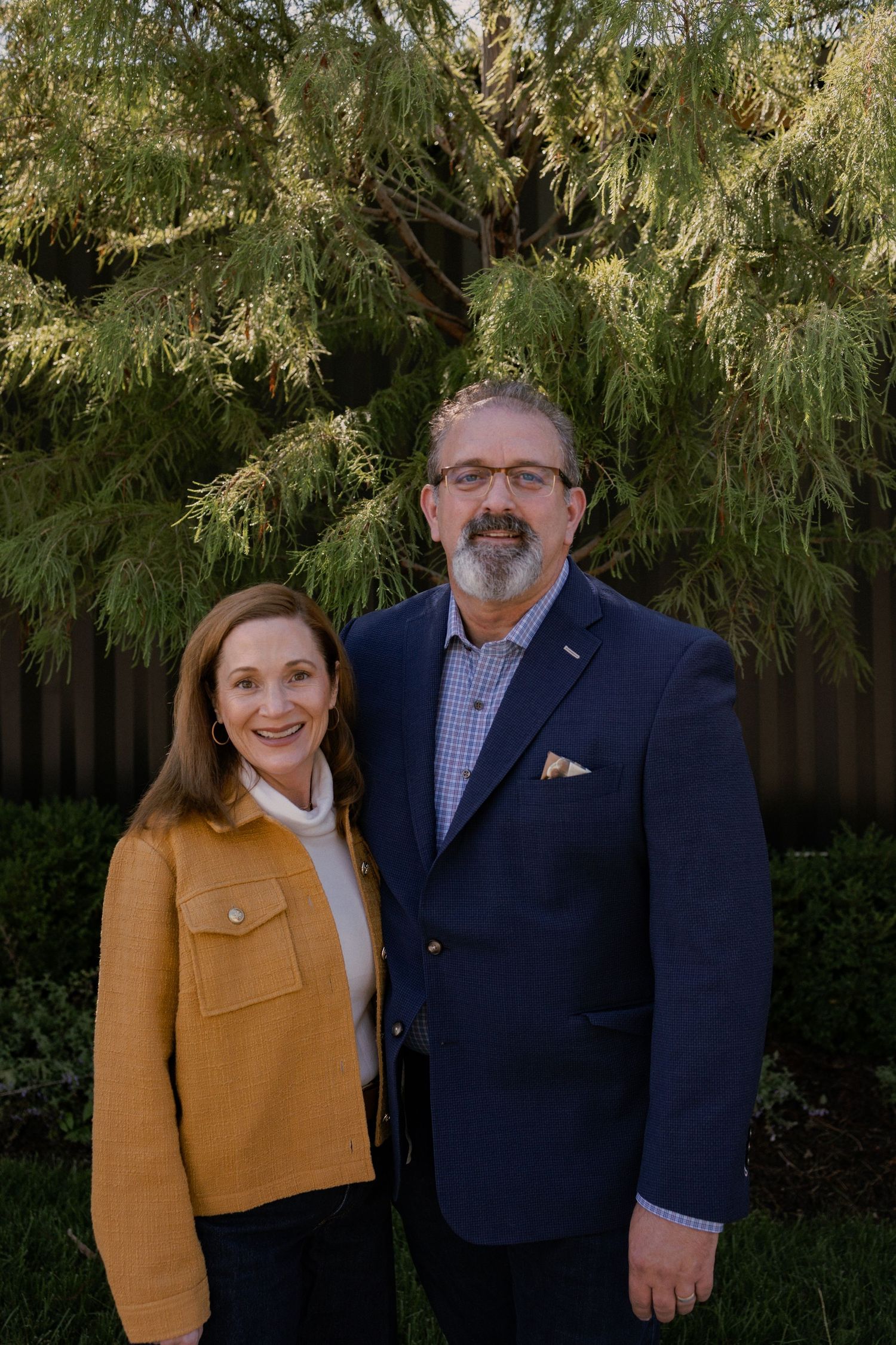 Couple in coordinating outfits pose together outdoors with trees in background.